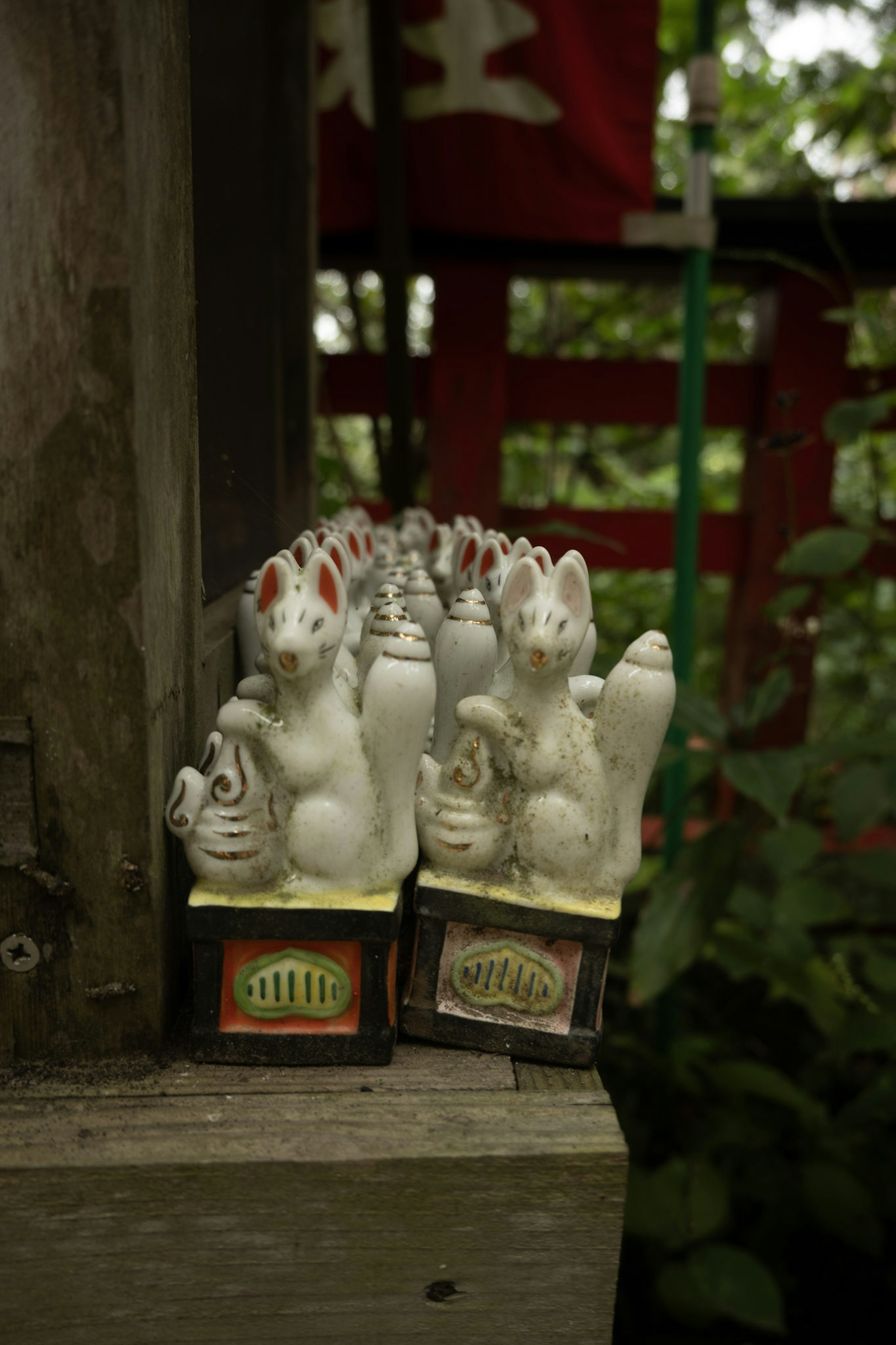 Una fila de figuras de zorro blancas con acentos rojos frente a una puerta de santuario tradicional