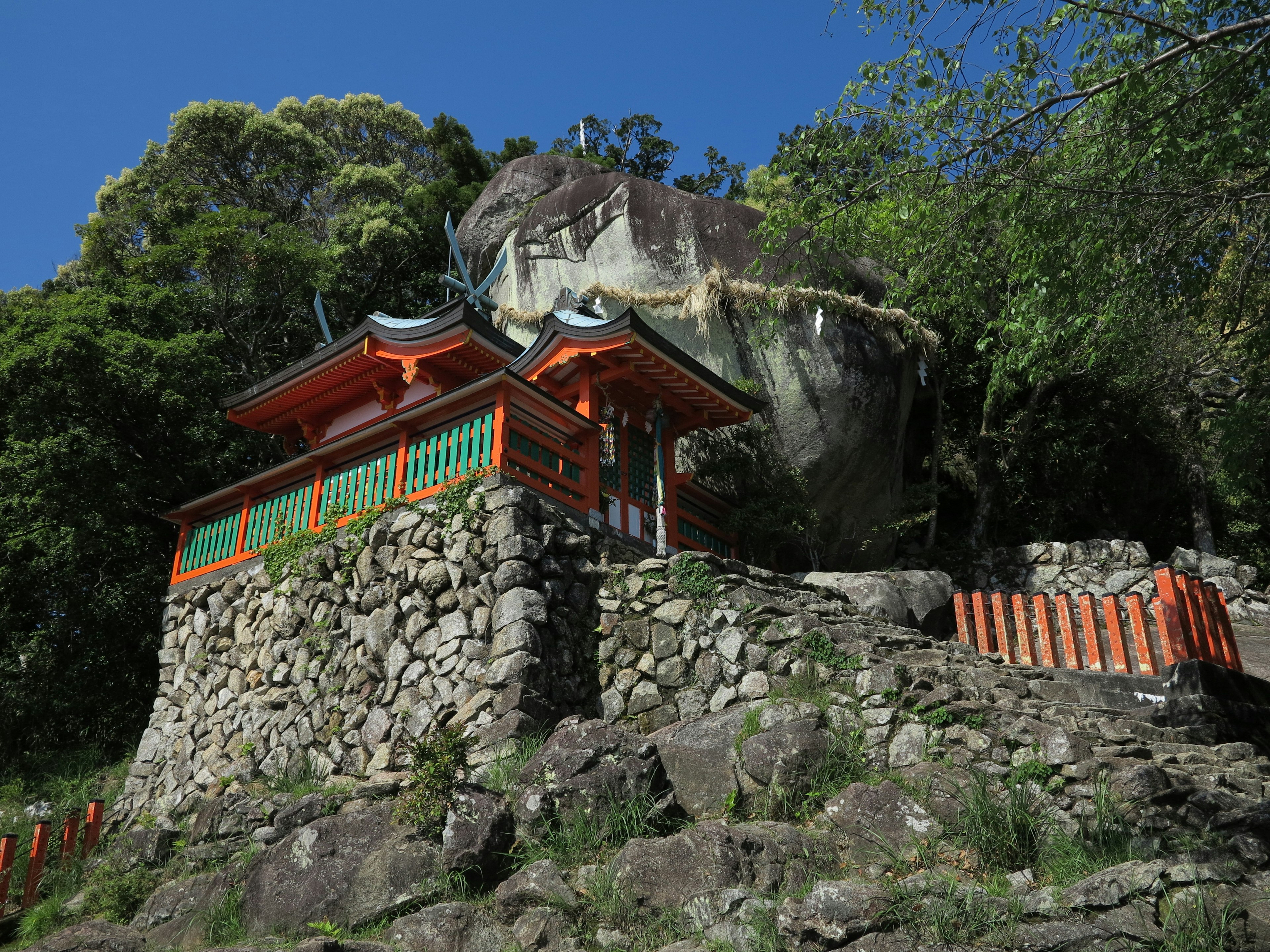 Un bâtiment de sanctuaire en orange et vert sur une colline rocheuse entourée de verdure