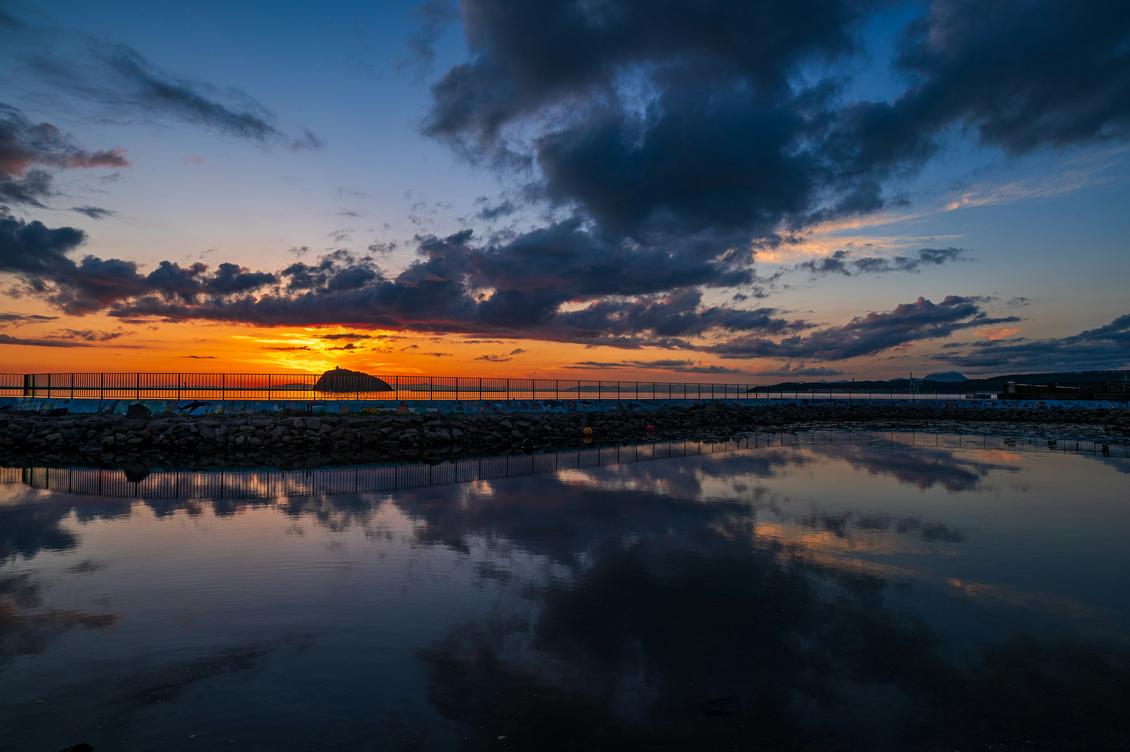 Vista escénica del atardecer reflejándose en el agua con nubes dramáticas