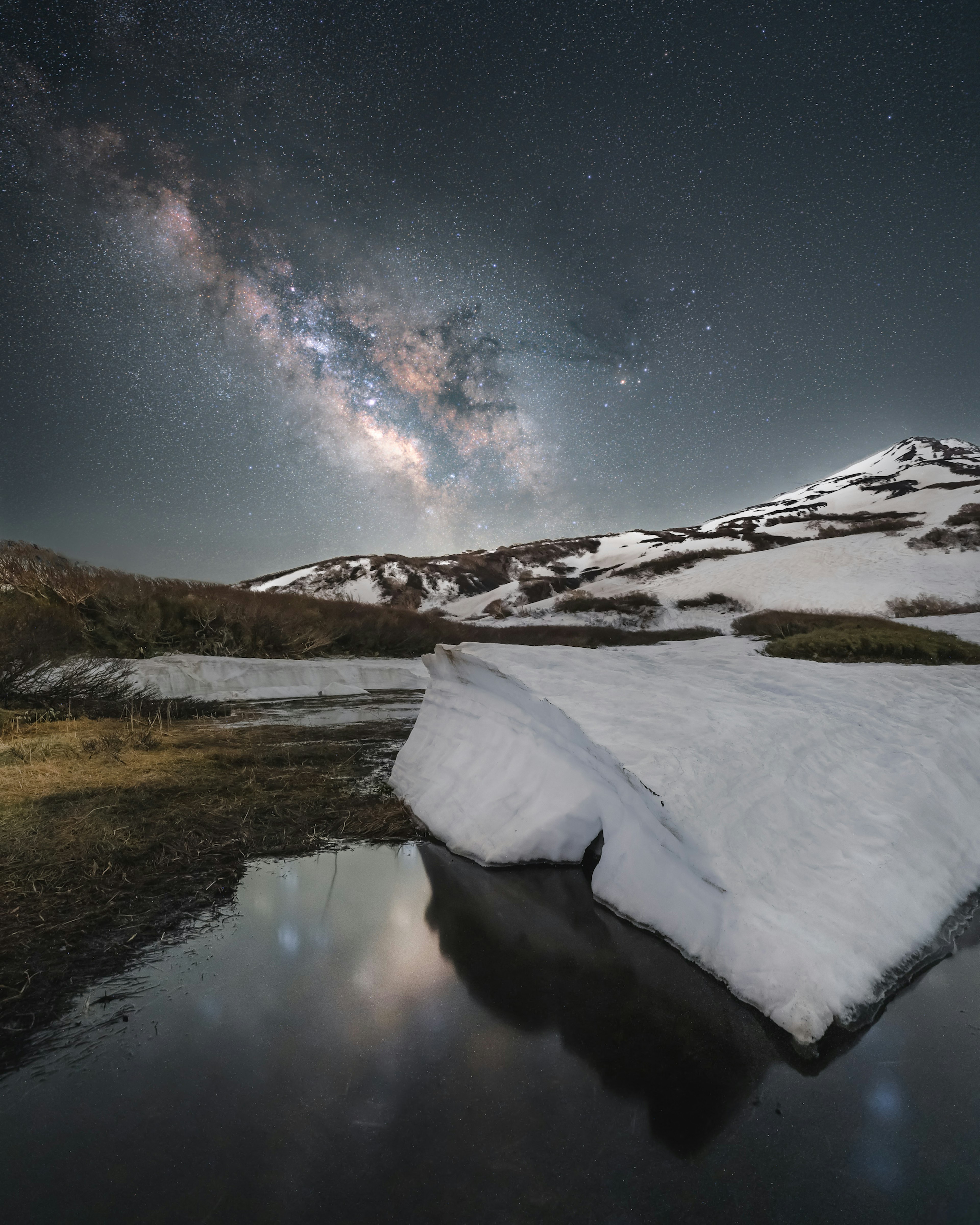 雪に覆われた山と星空の下の水面に映るミルキーウェイ