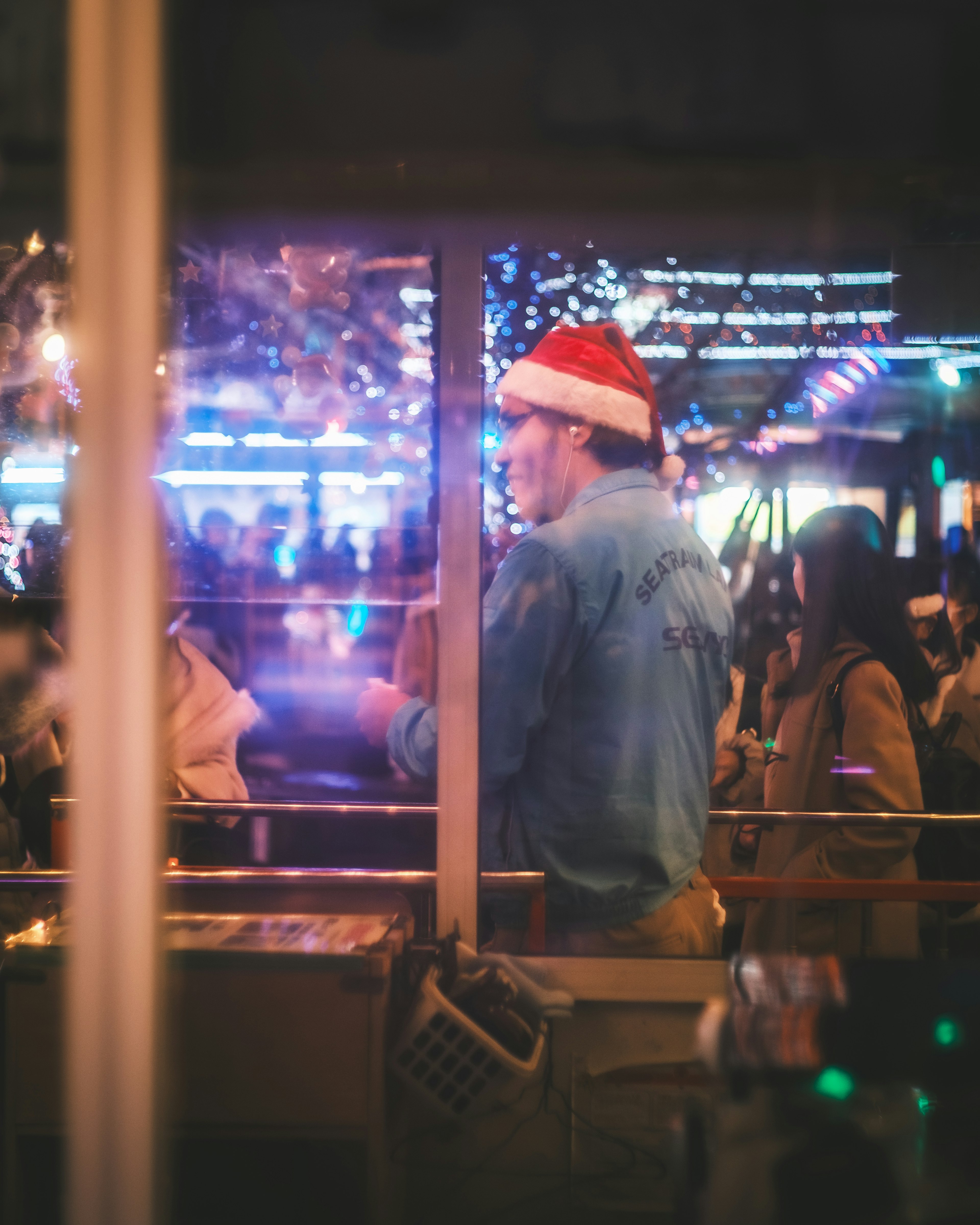 Man wearing a Santa hat looking out of a window at a festive night scene