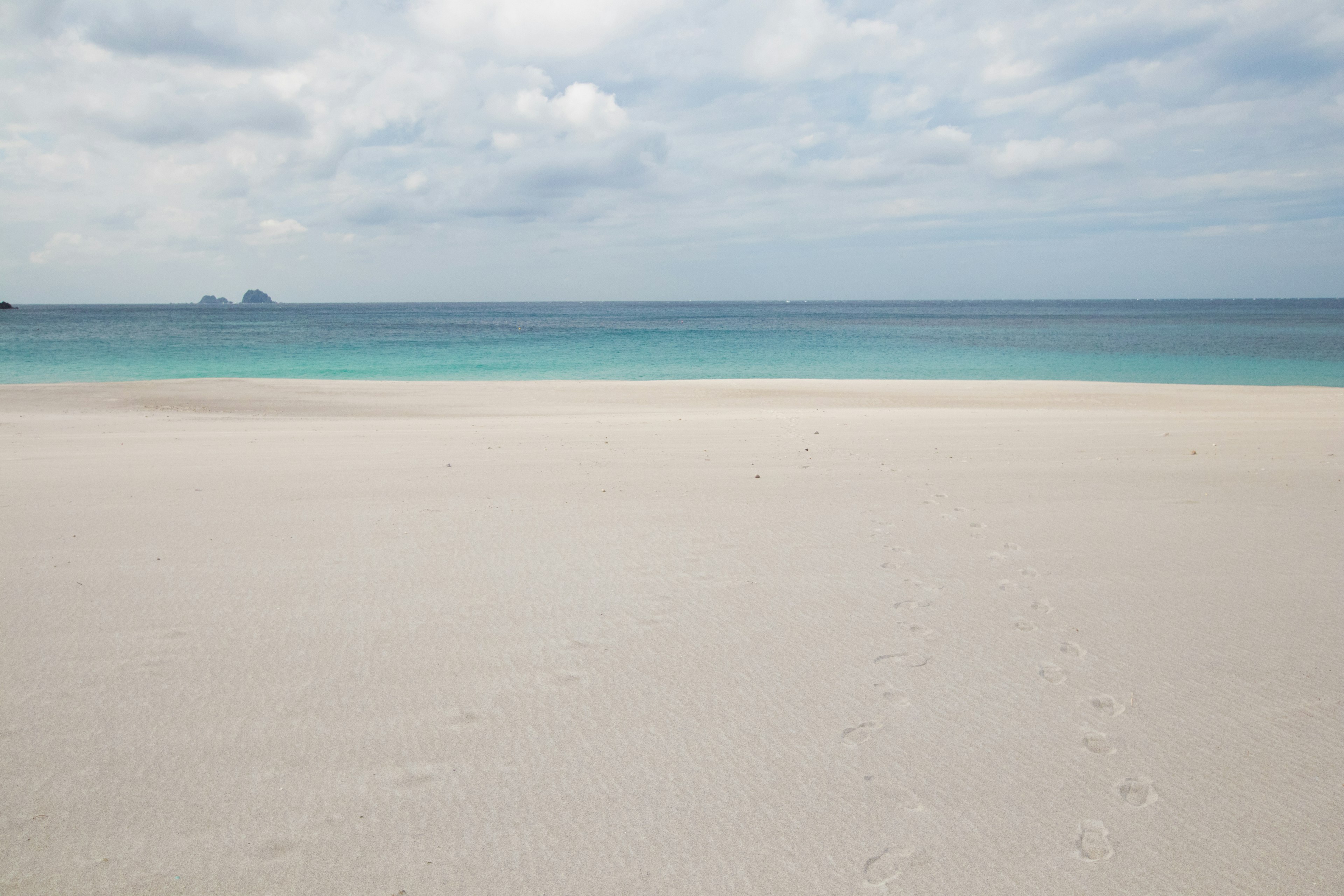 Ruhiges Meer und weißer Sandstrand unter einem bewölkten Himmel