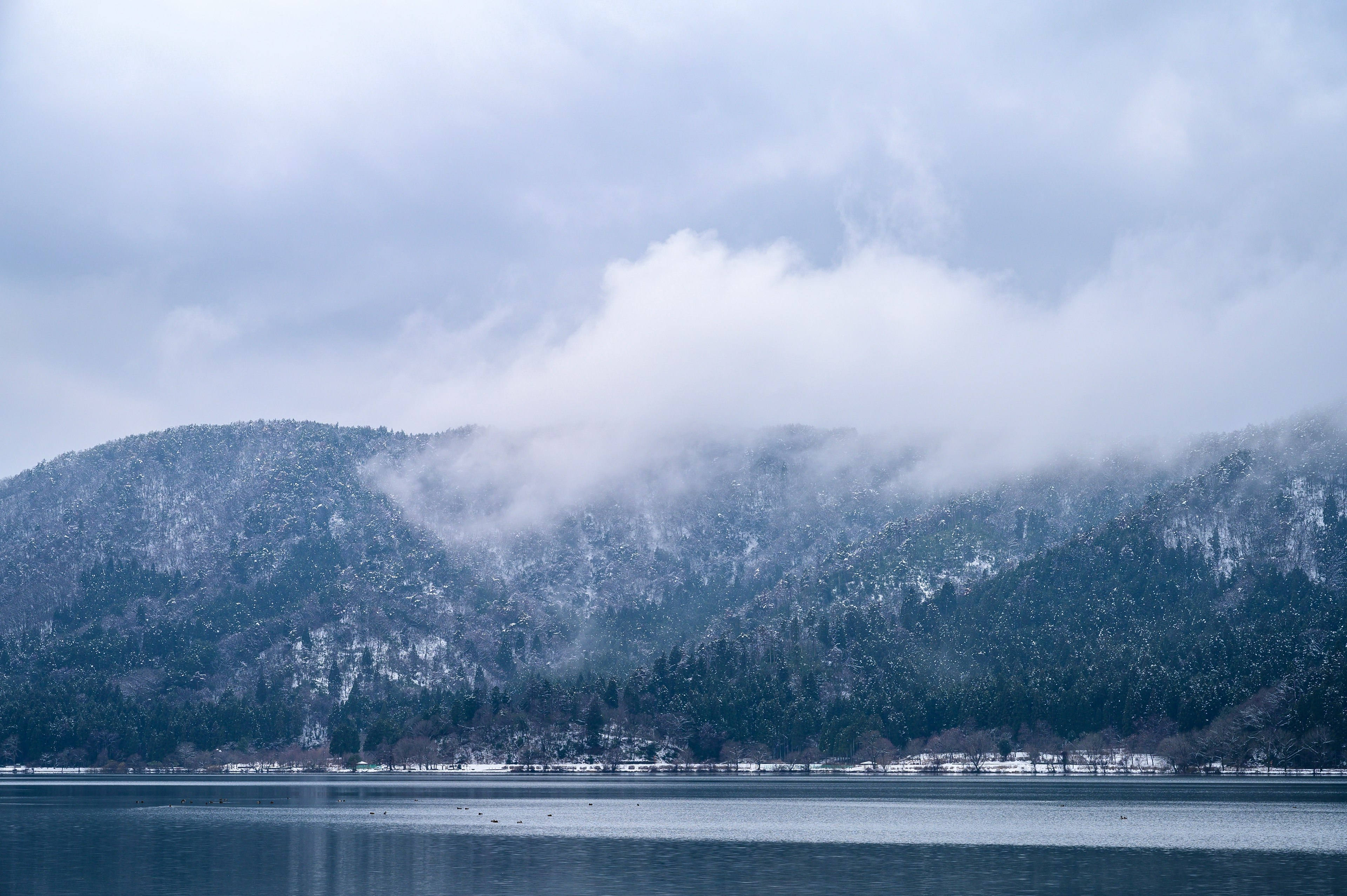 雪に覆われた山々と雲がかかる静かな湖の風景