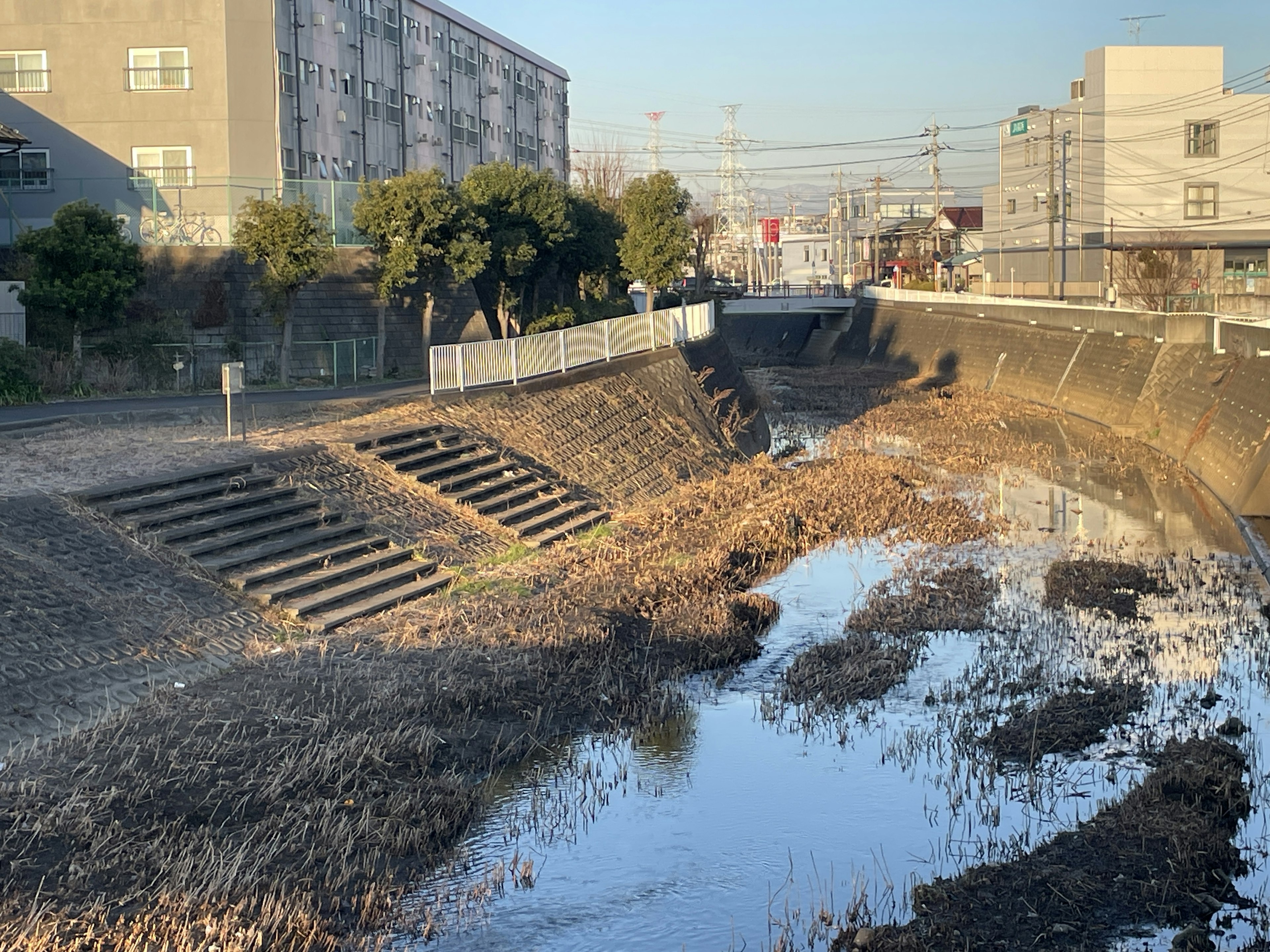 A dry riverbed with sparse water and nearby buildings