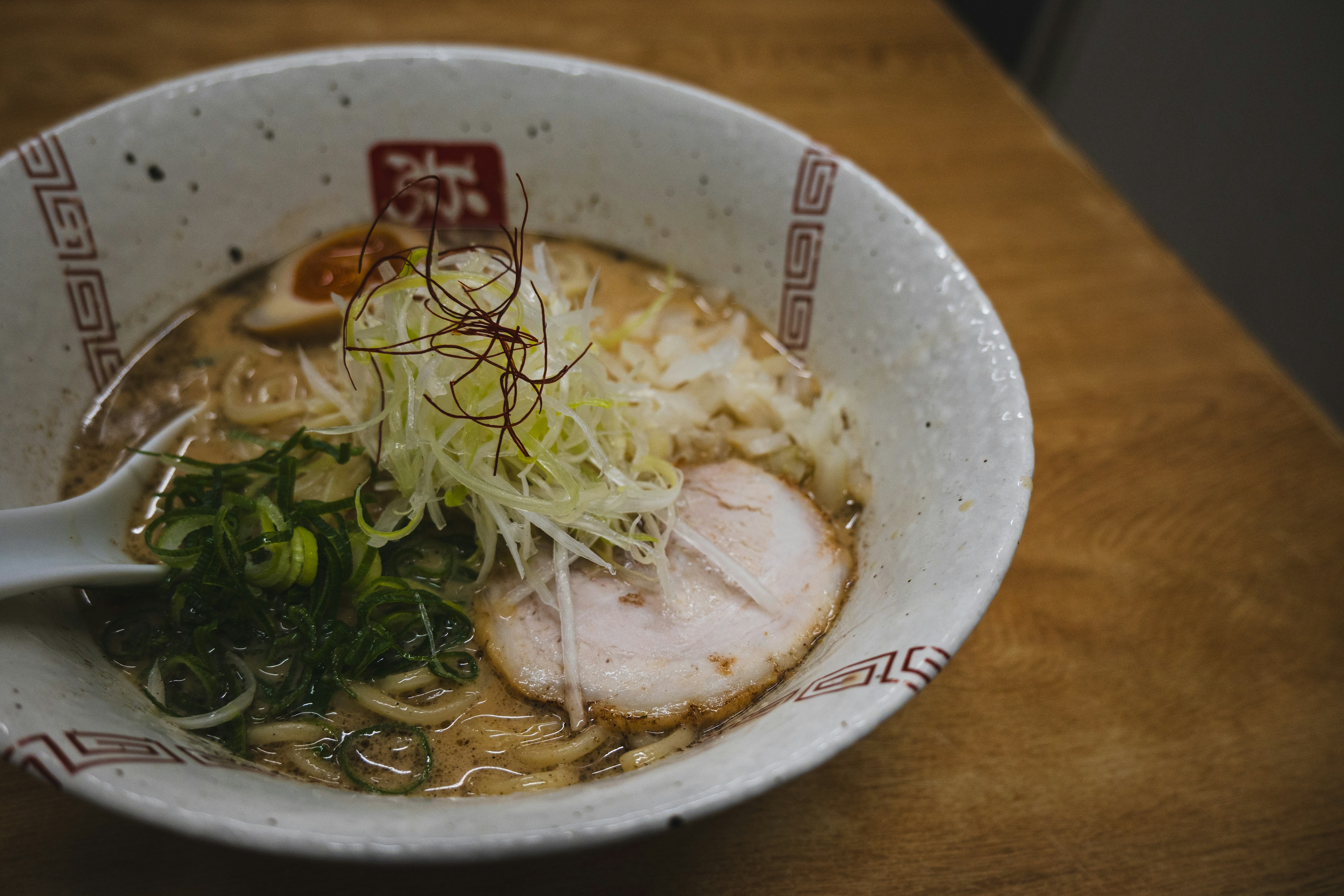 ラーメンのボウルにスライスされたチャーシューとネギがトッピングされている