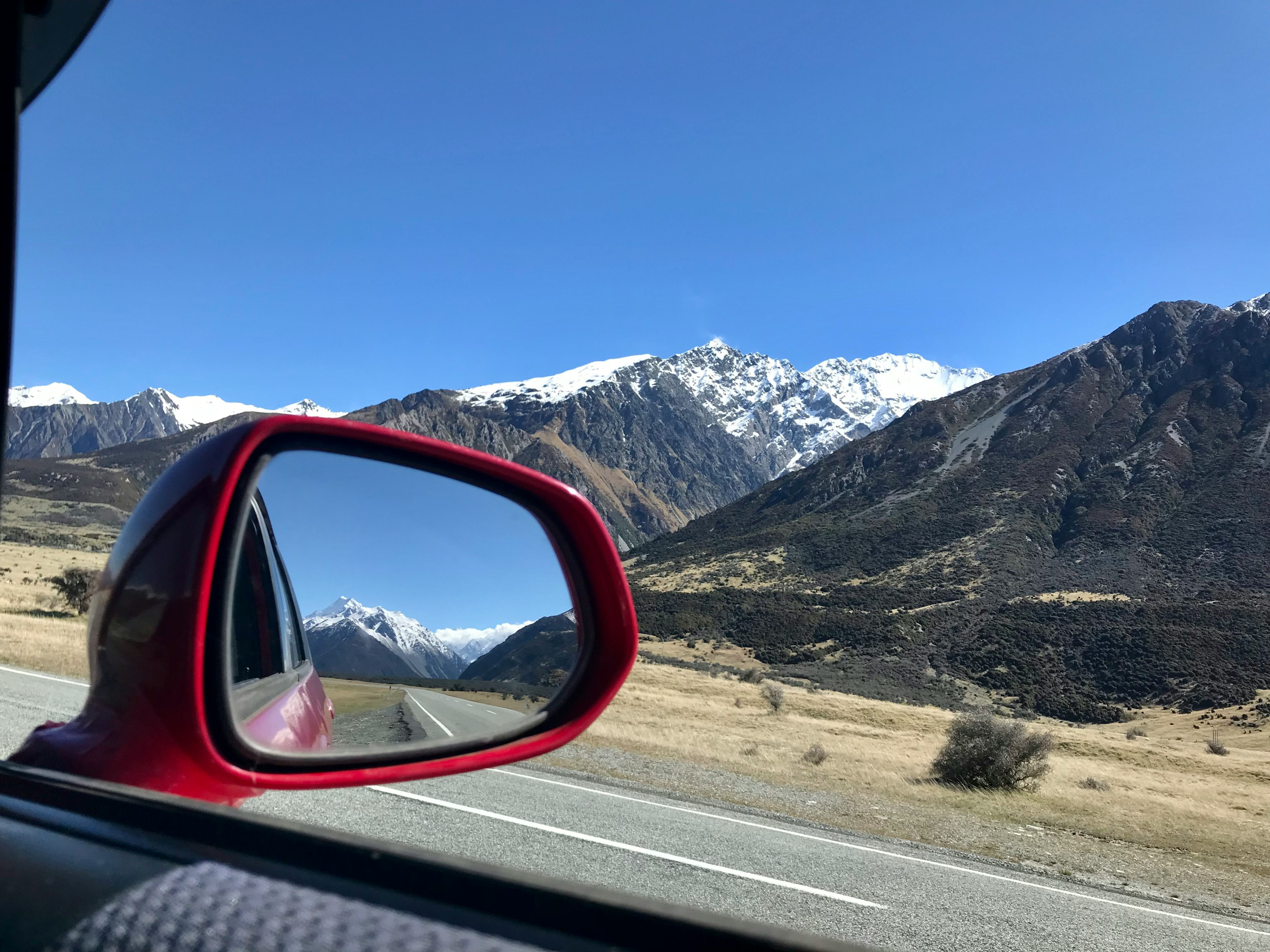 Montañas cubiertas de nieve y cielo azul reflejados en un espejo lateral de coche