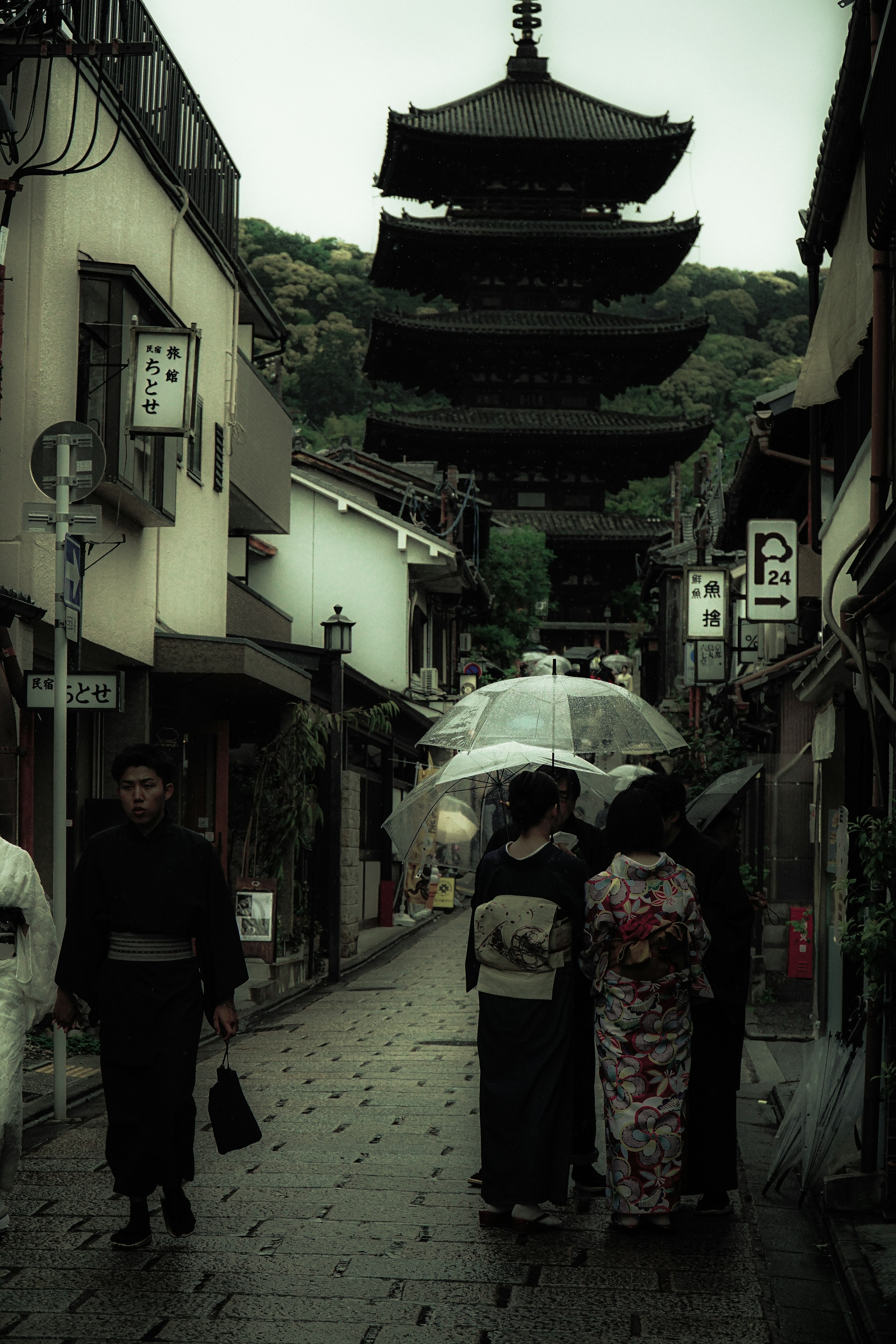 Dos personas en kimono caminando bajo un paraguas en la lluvia con una pagoda al fondo