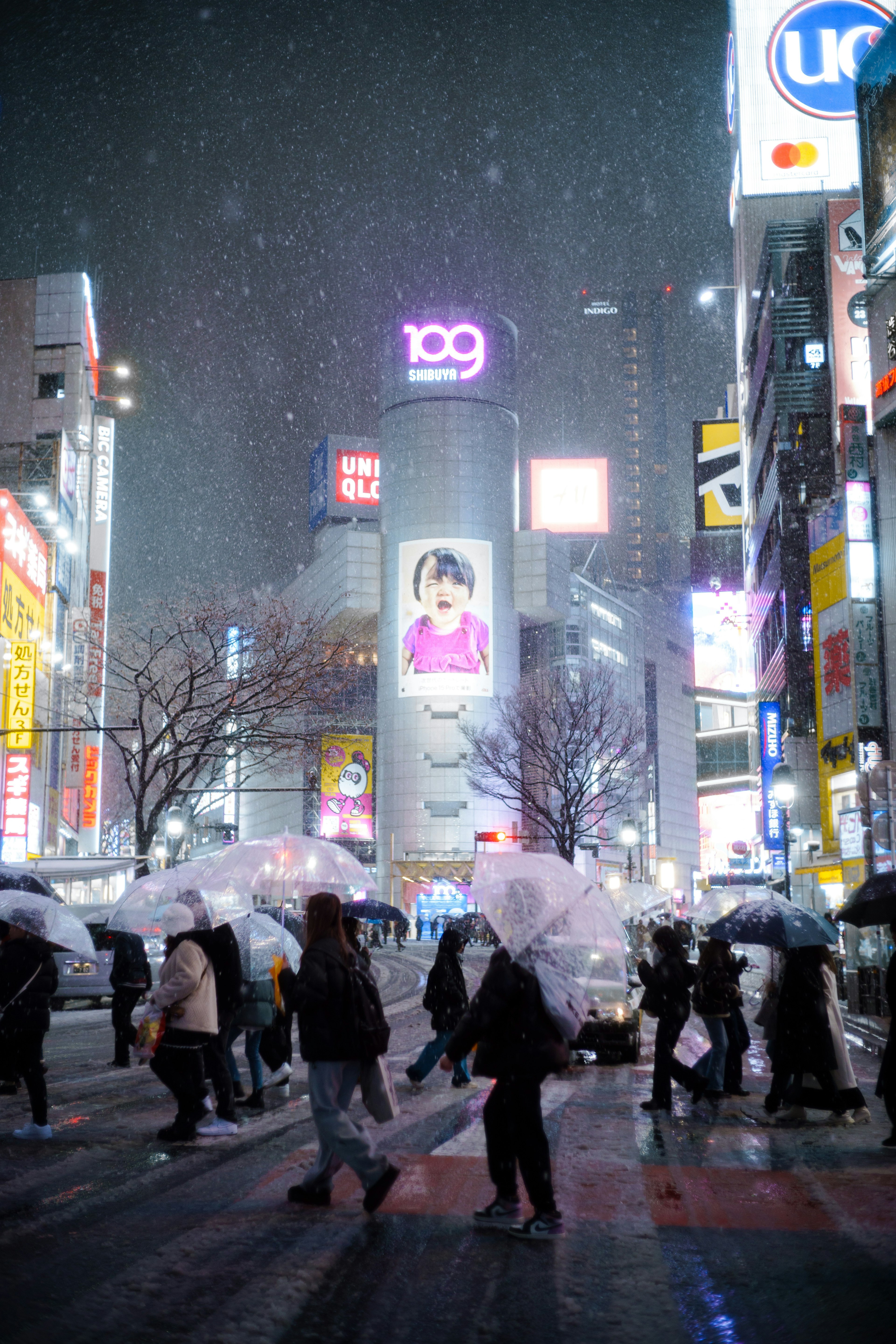 雪の降る夜の渋谷交差点で傘を持った人々が横断している