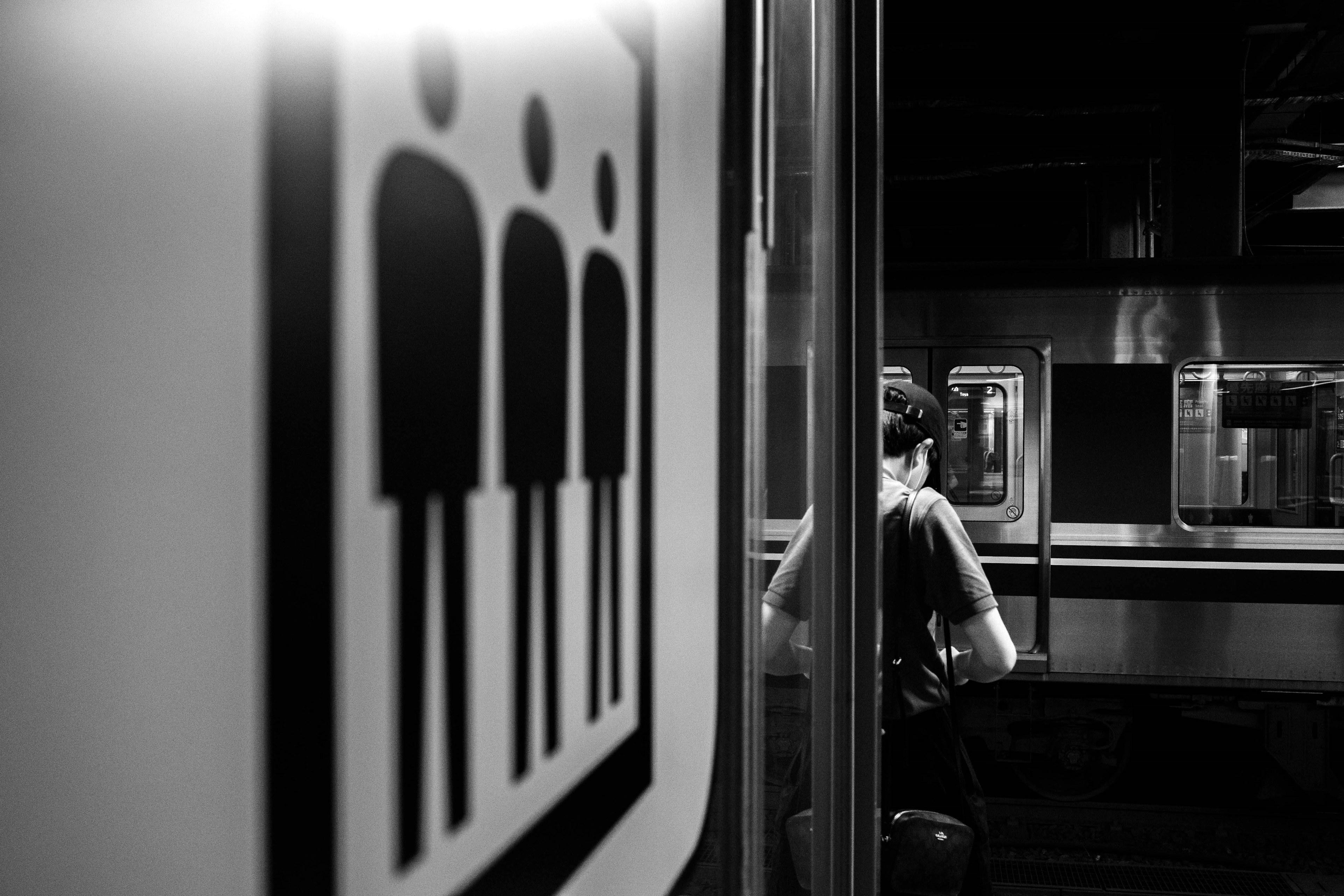 Black and white image of a sign indicating people and an individual in the background