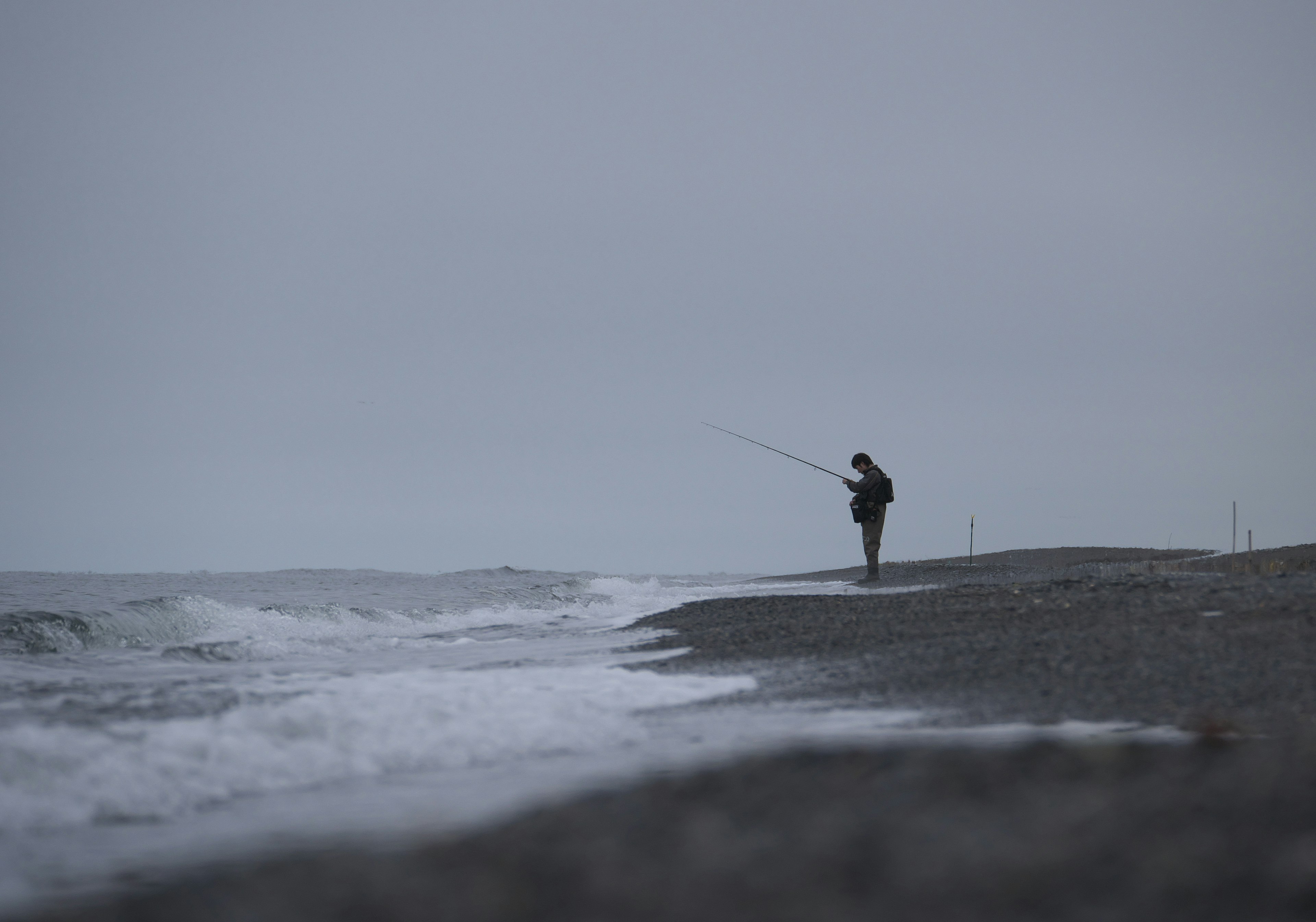 Silhouette of a person fishing on a gray beach landscape