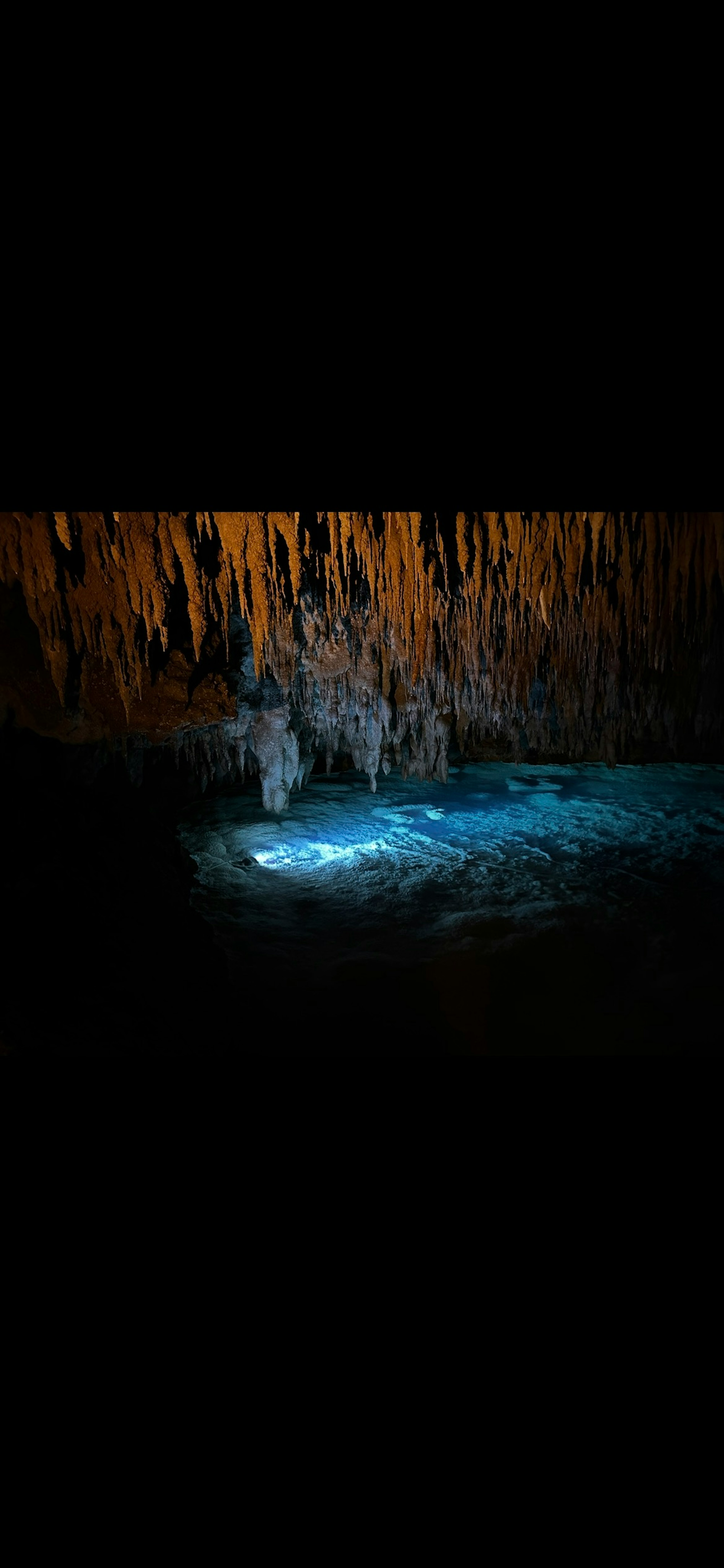 Interior de cueva con agua azul y estalactitas naranjas