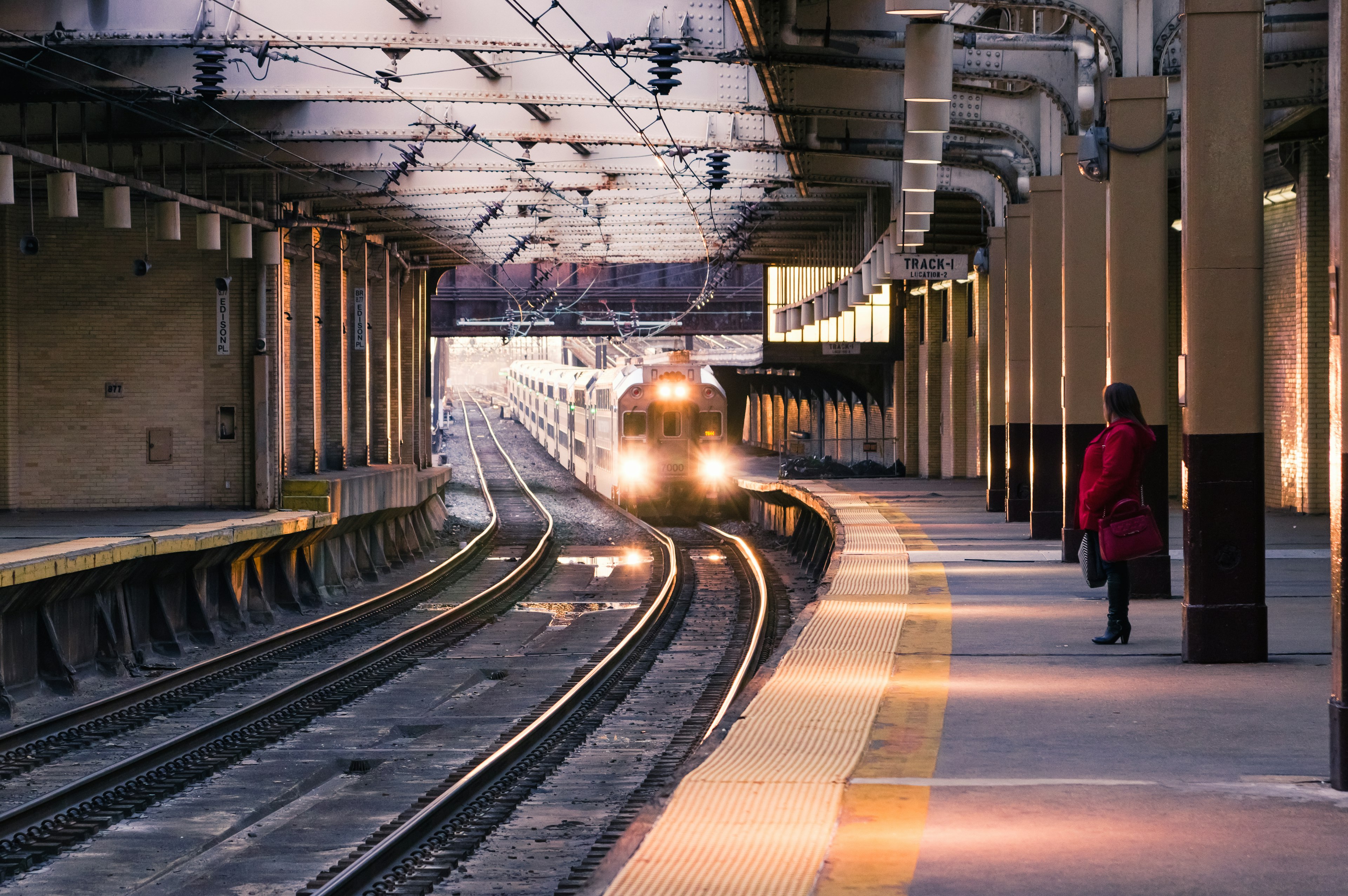 Treno in arrivo su una banchina con una persona in cappotto rosso in attesa