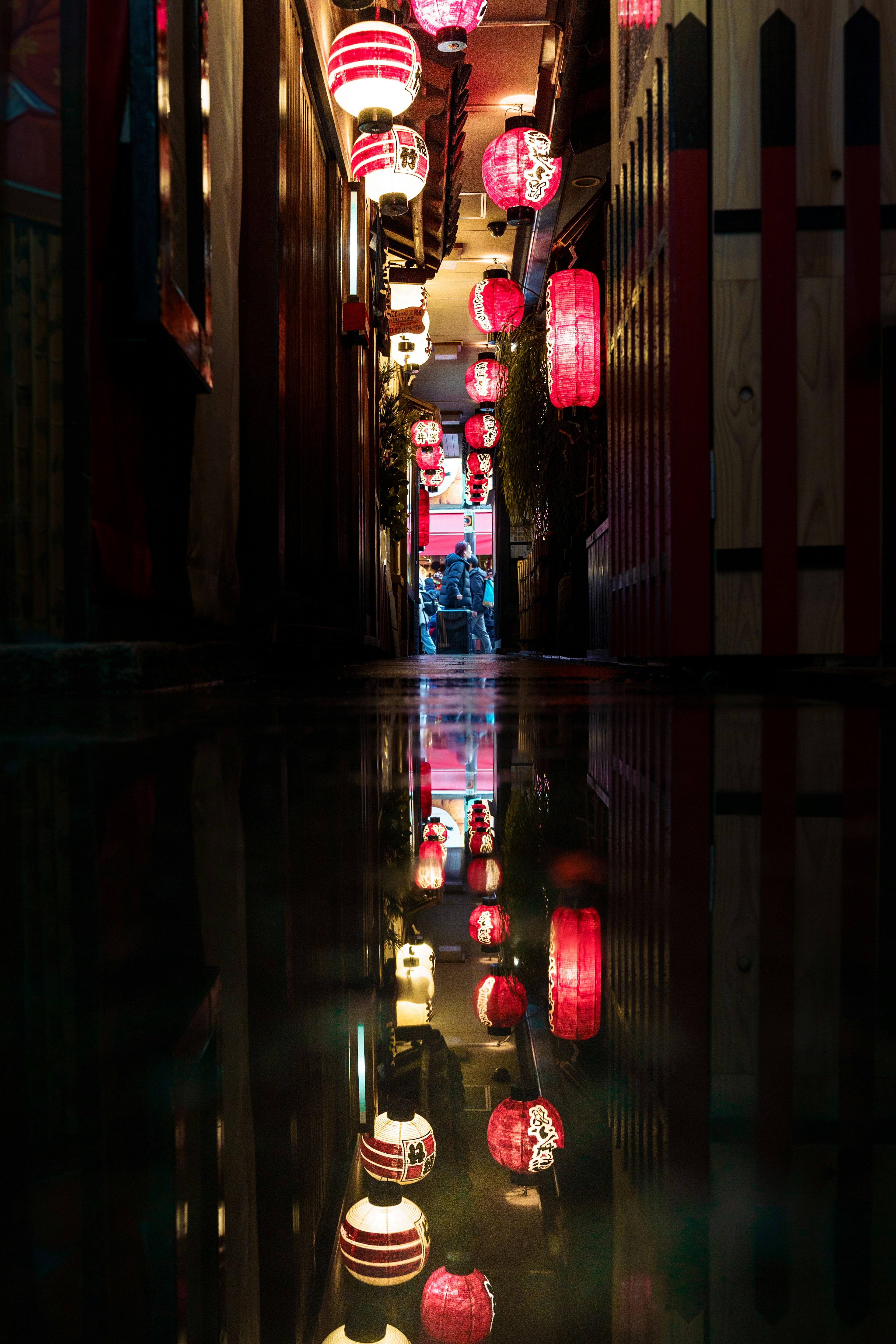 Callejón estrecho con faroles rojos reflejados en el agua