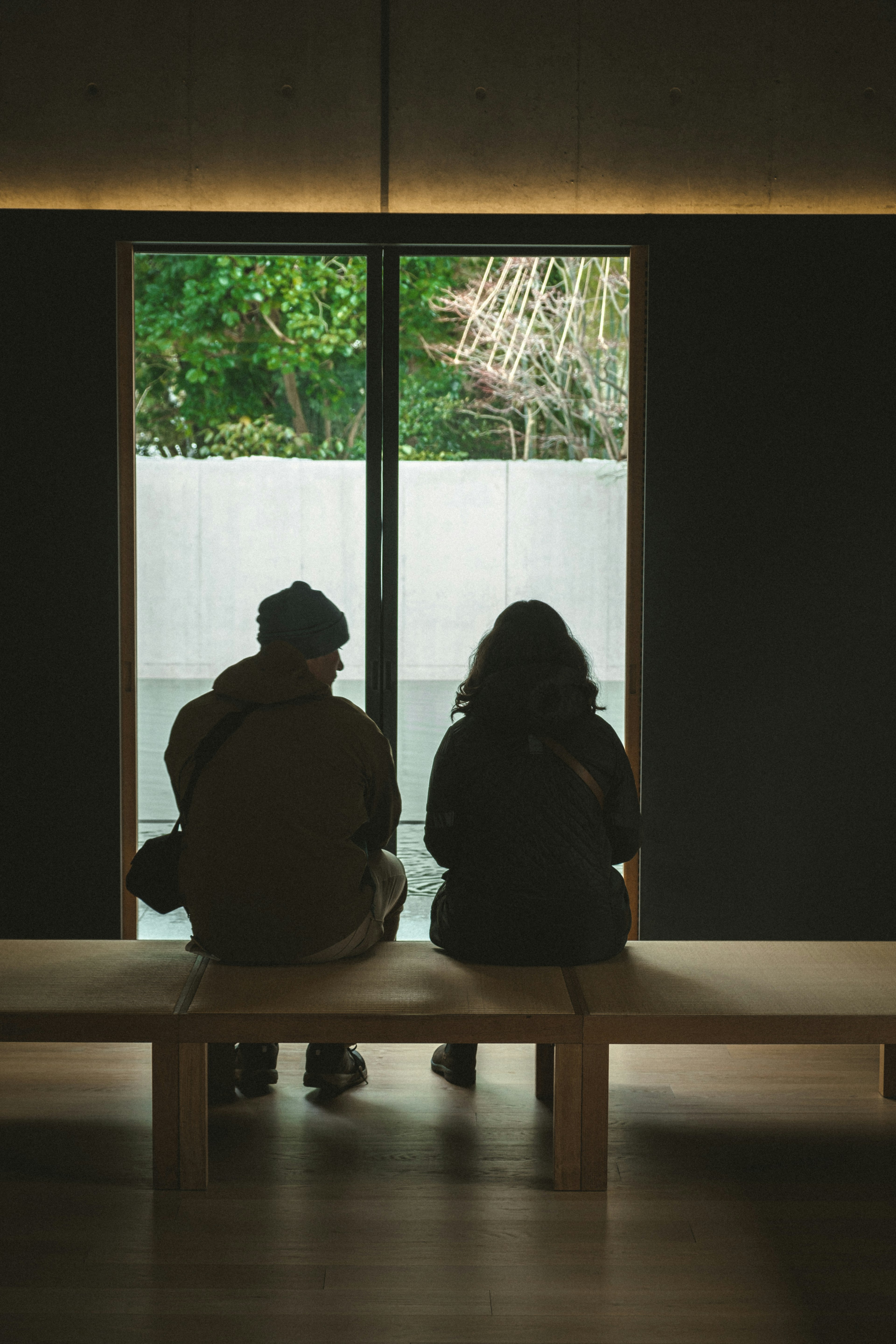 Silhouette von zwei Personen, die an einem Fenster mit Blick auf das Grün sitzen