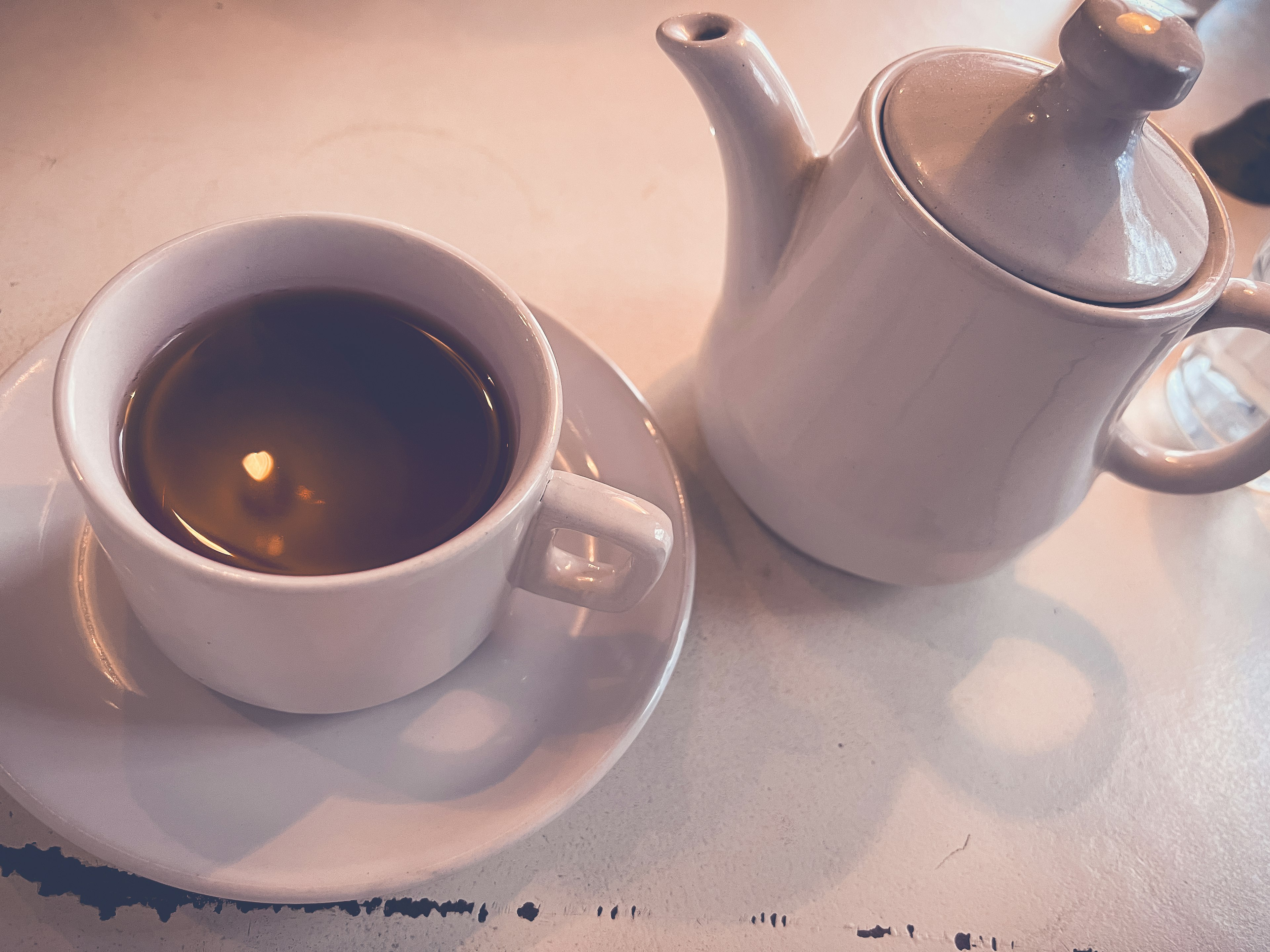 A white teapot next to a coffee cup on a table