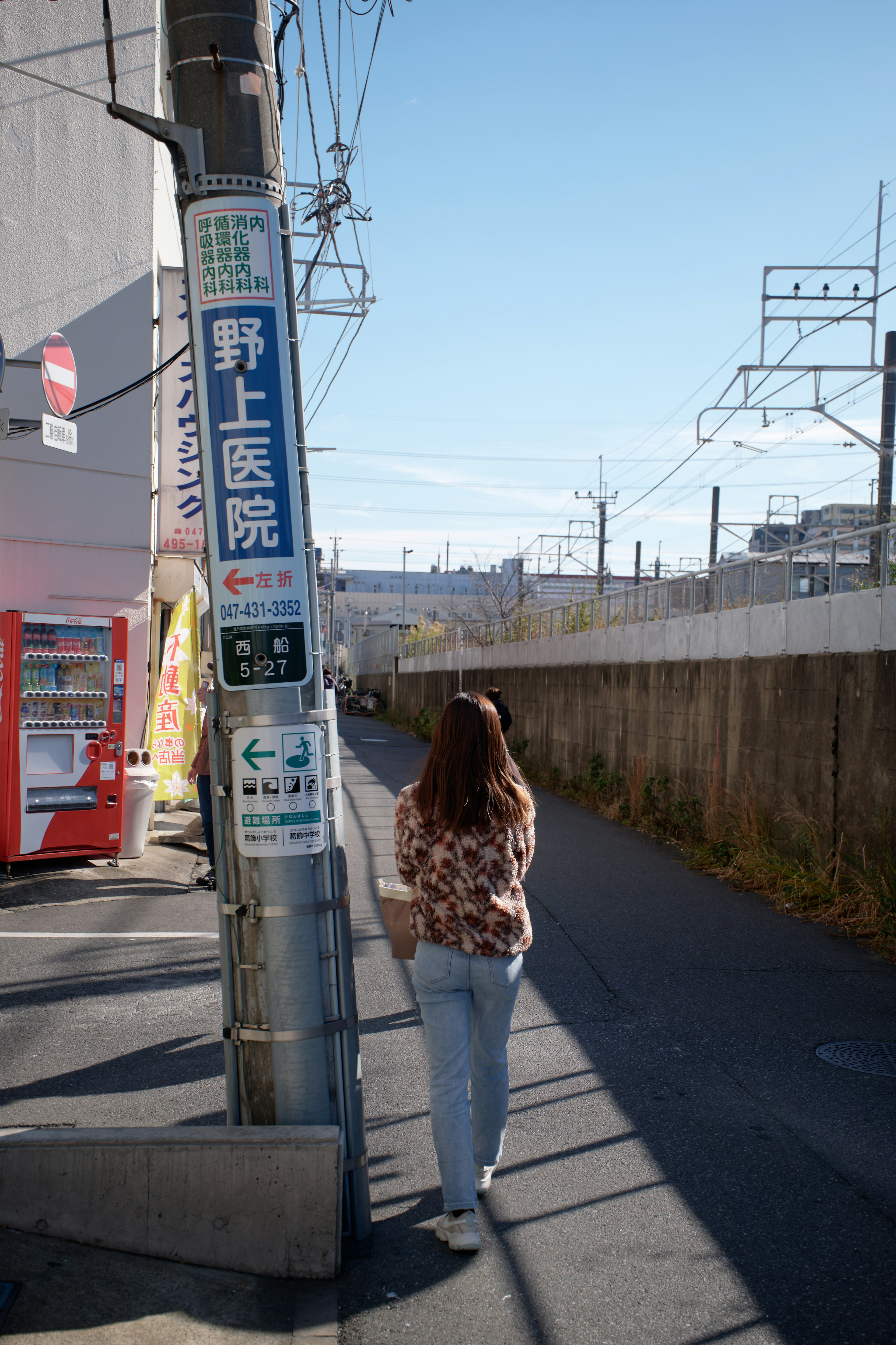 Eine Frau, die auf einem Weg mit klarem blauen Himmel und Bahngleisen im Hintergrund geht