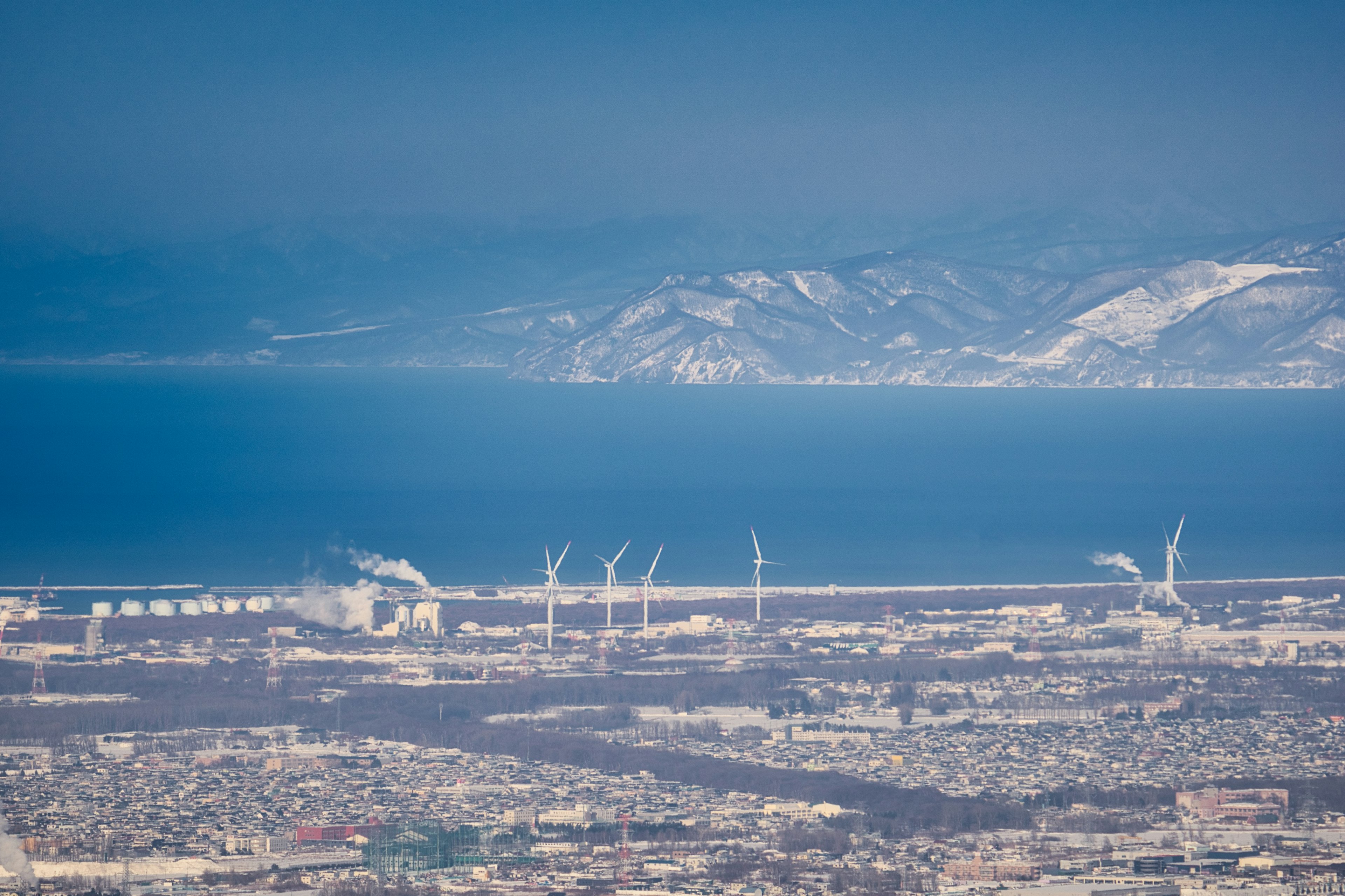 Luftaufnahme einer Küstenstadt mit Windkraftanlagen und blauem Ozean