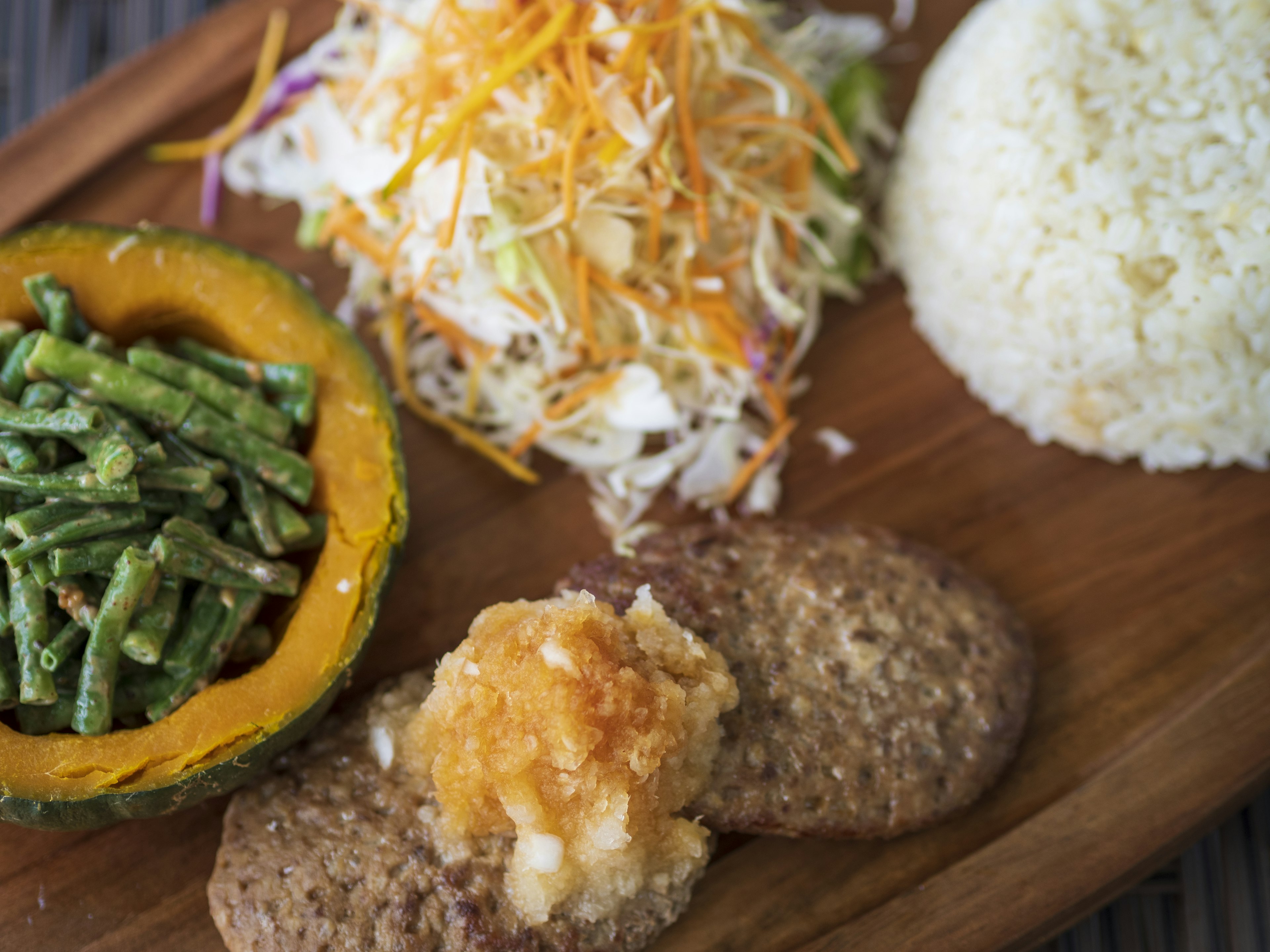 A plate featuring colorful salad, rice, pumpkin, and green bean dish