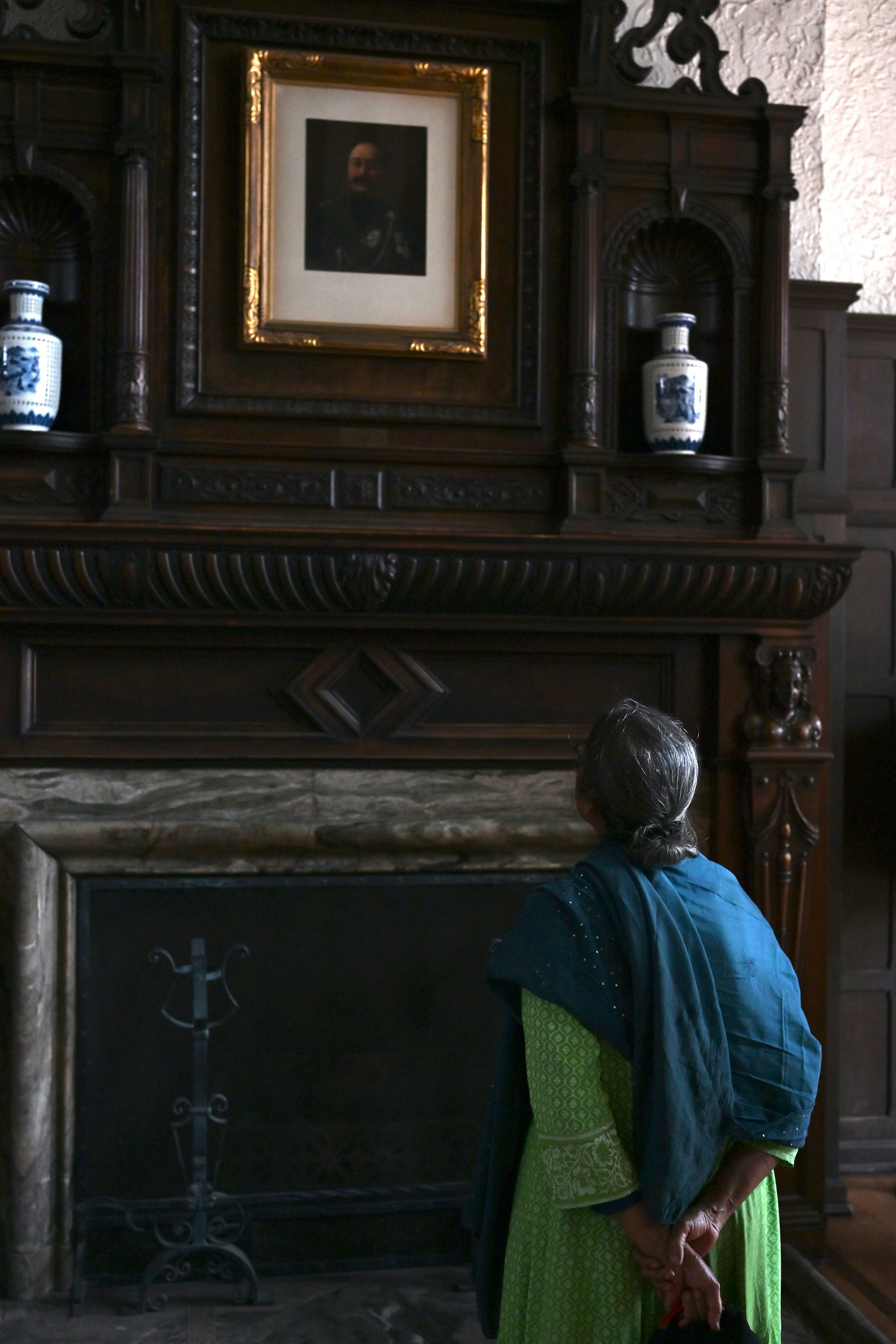 A woman admiring a painting in front of a fireplace