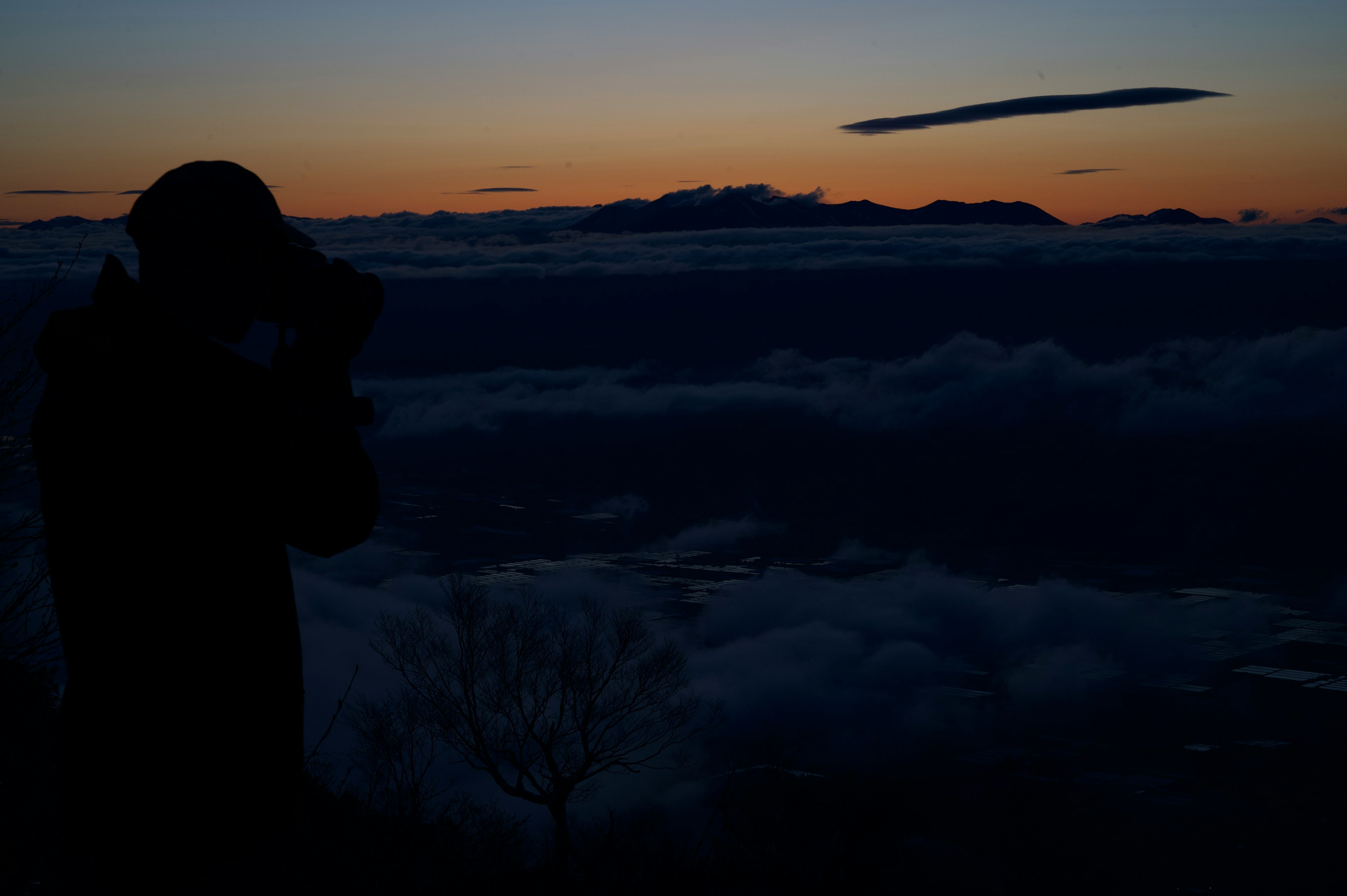 夕日を背景にカメラを構えるシルエットの人