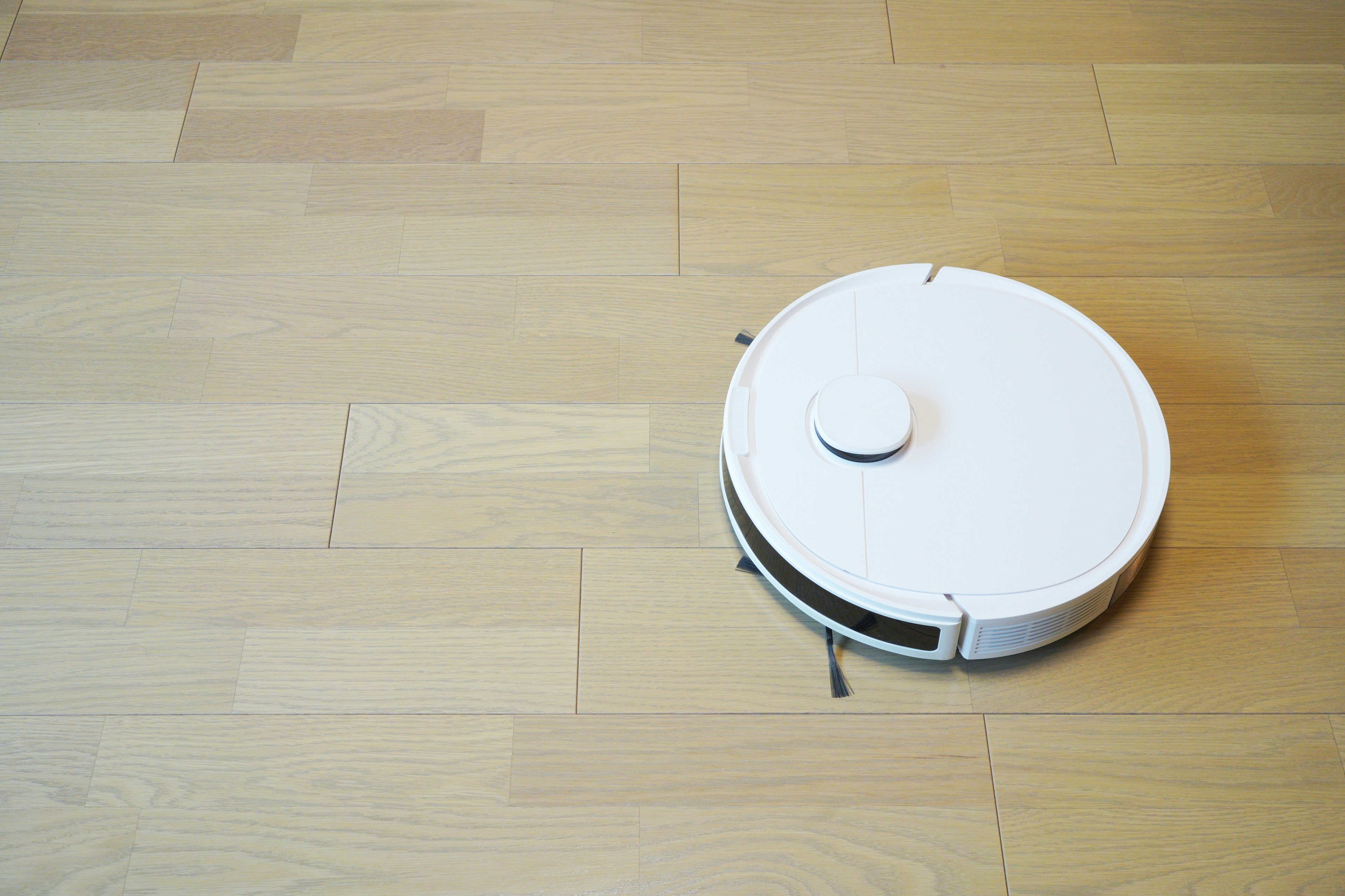 A white robotic vacuum cleaner moving on a wooden floor