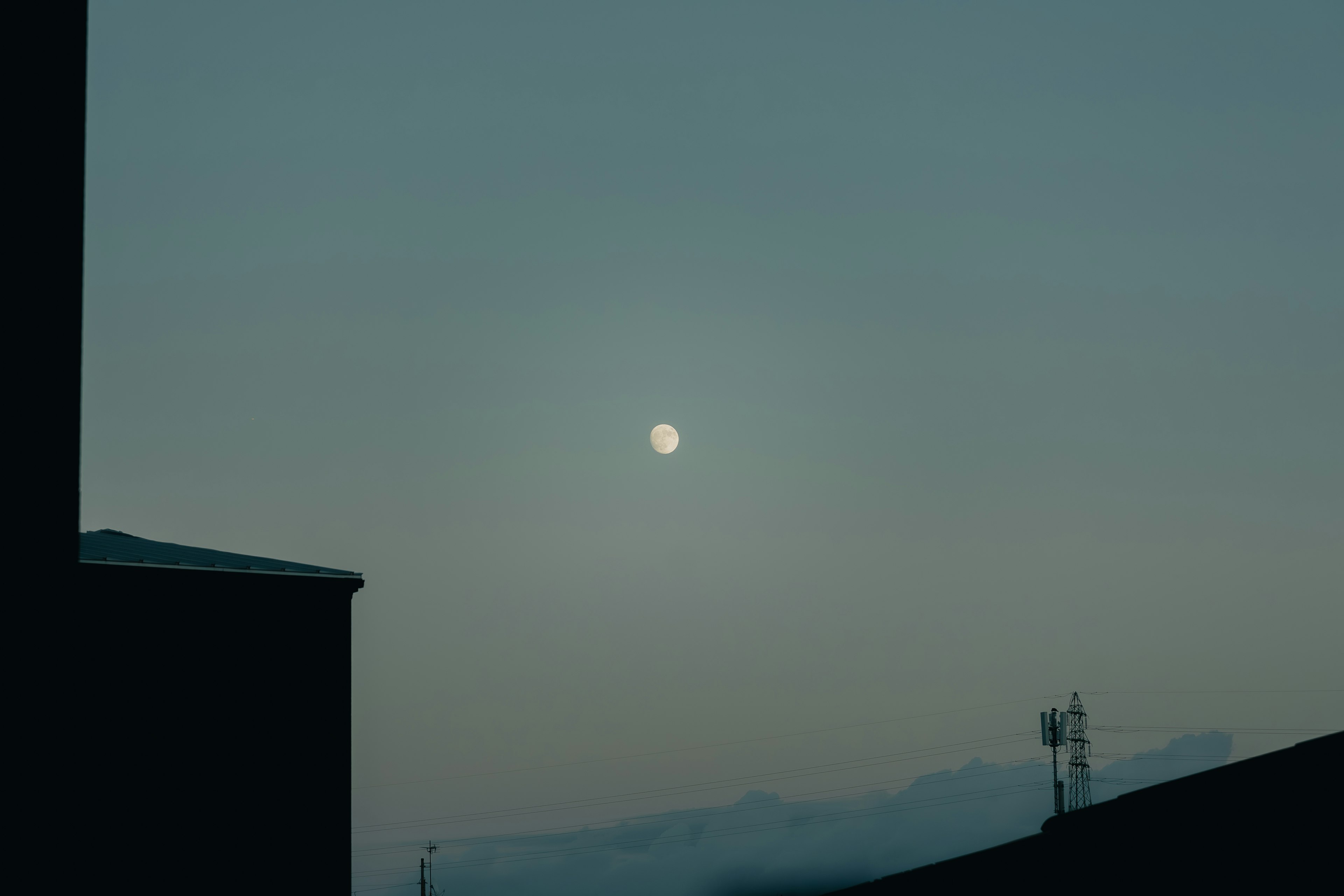 Moon in a twilight sky with silhouetted buildings