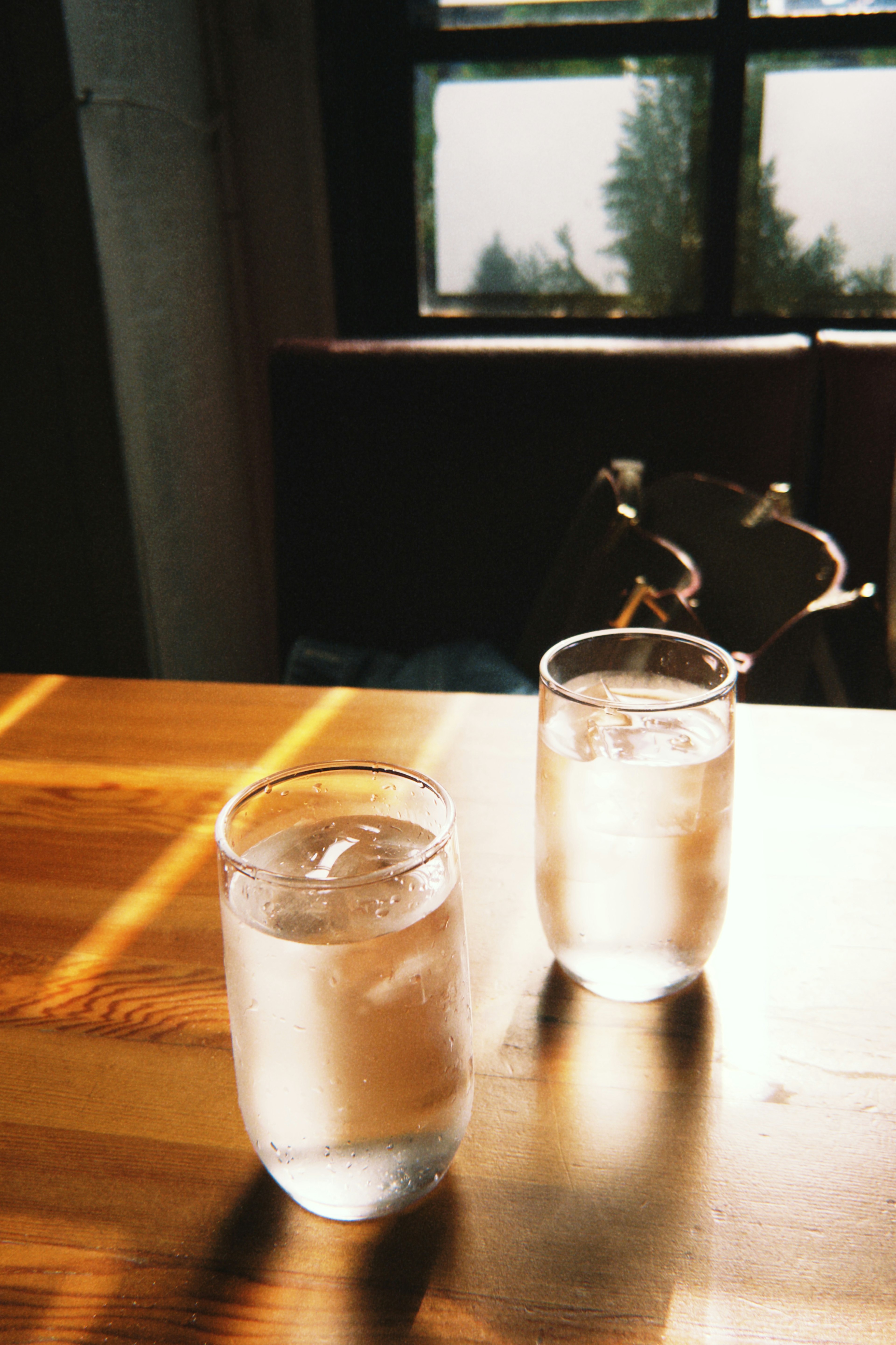 Dos vasos de agua helada sobre una mesa de madera con luz natural que entra por una ventana