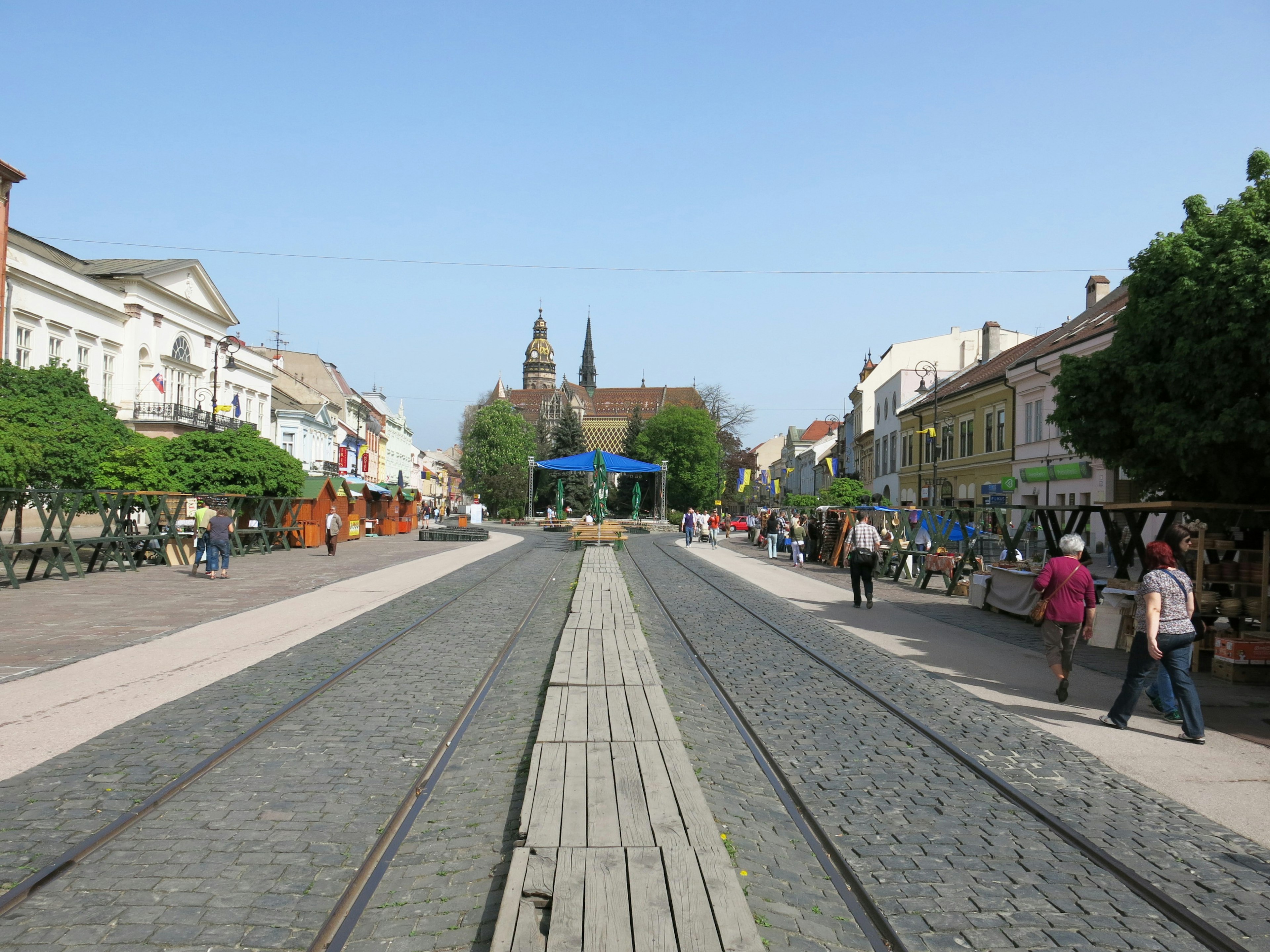 A scenic view of a street with railway tracks and people walking