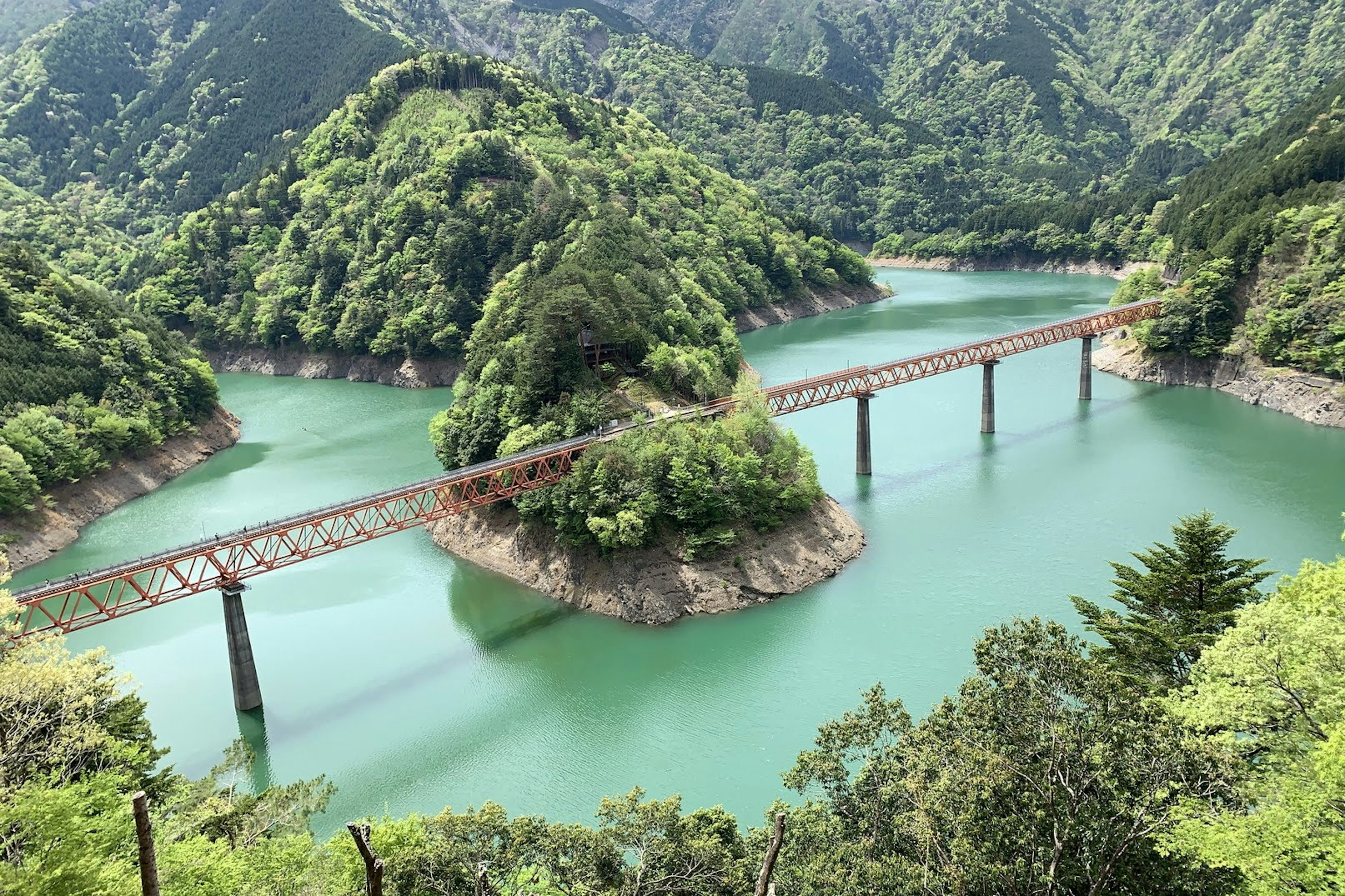 A scenic view of a lake surrounded by lush green mountains and a bridge