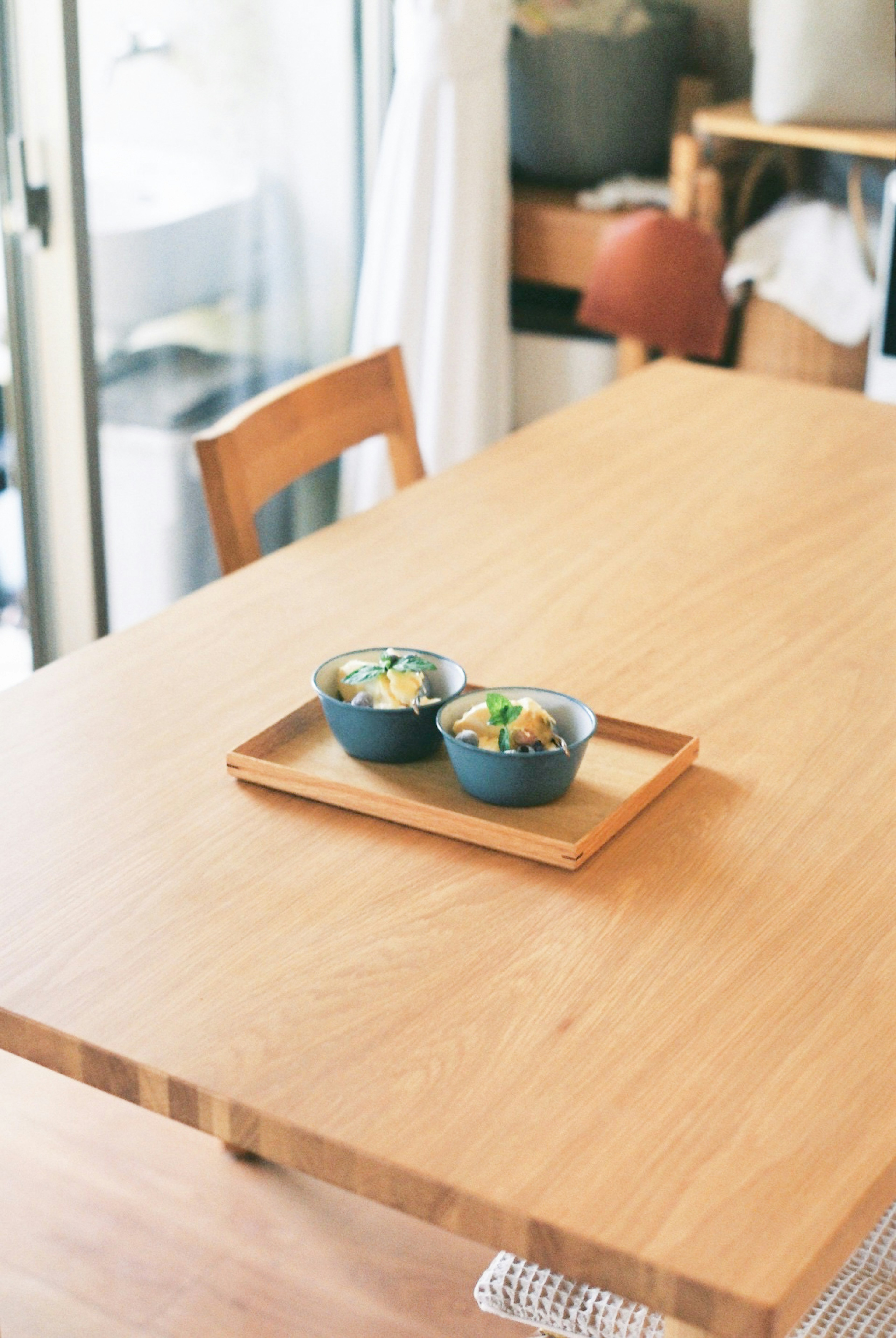 Mesa de comedor simple con superficie de madera que presenta dos cuencos azules de comida en una bandeja de madera