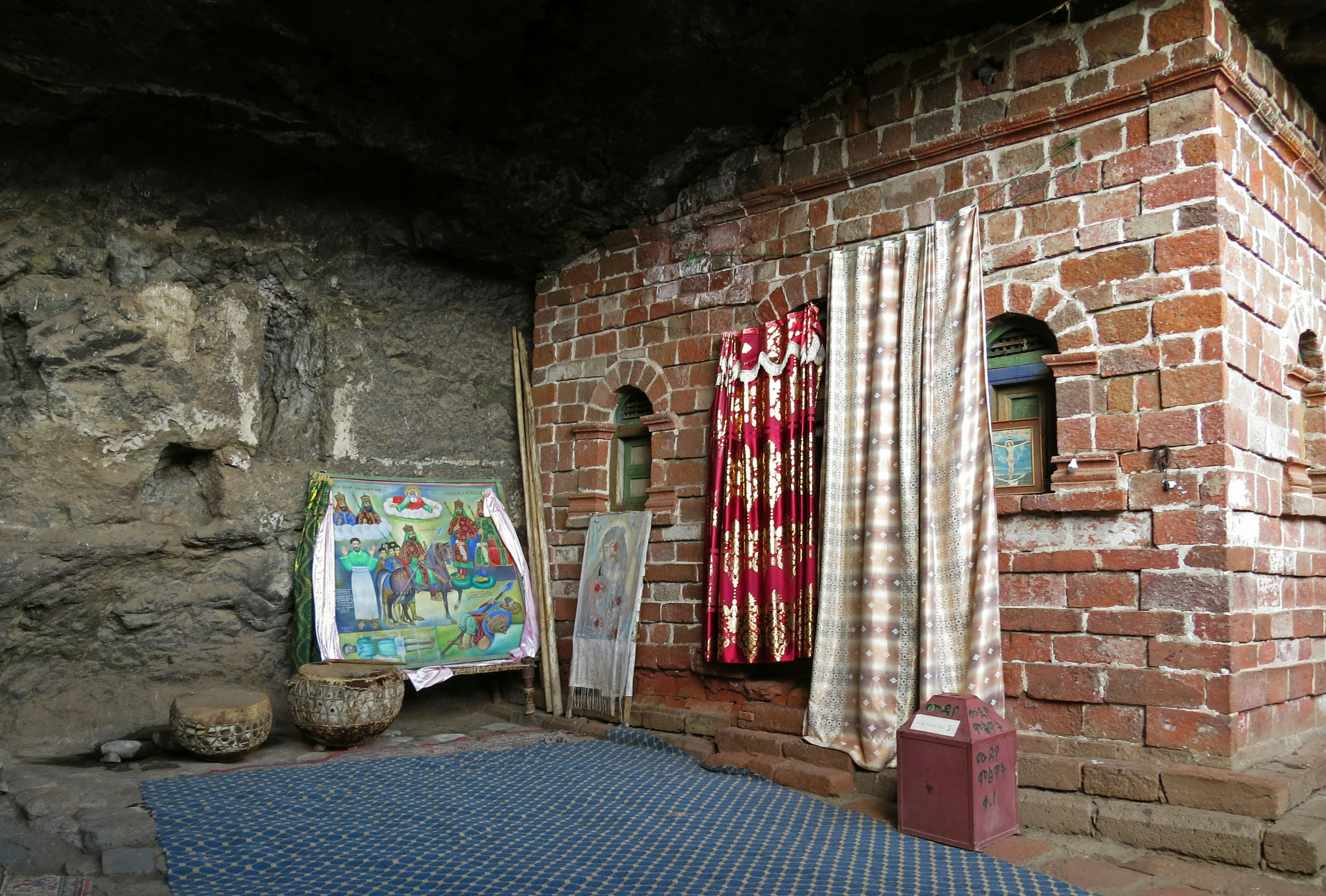 Estructura de ladrillo con cortinas y una pintura dentro de una cueva rocosa