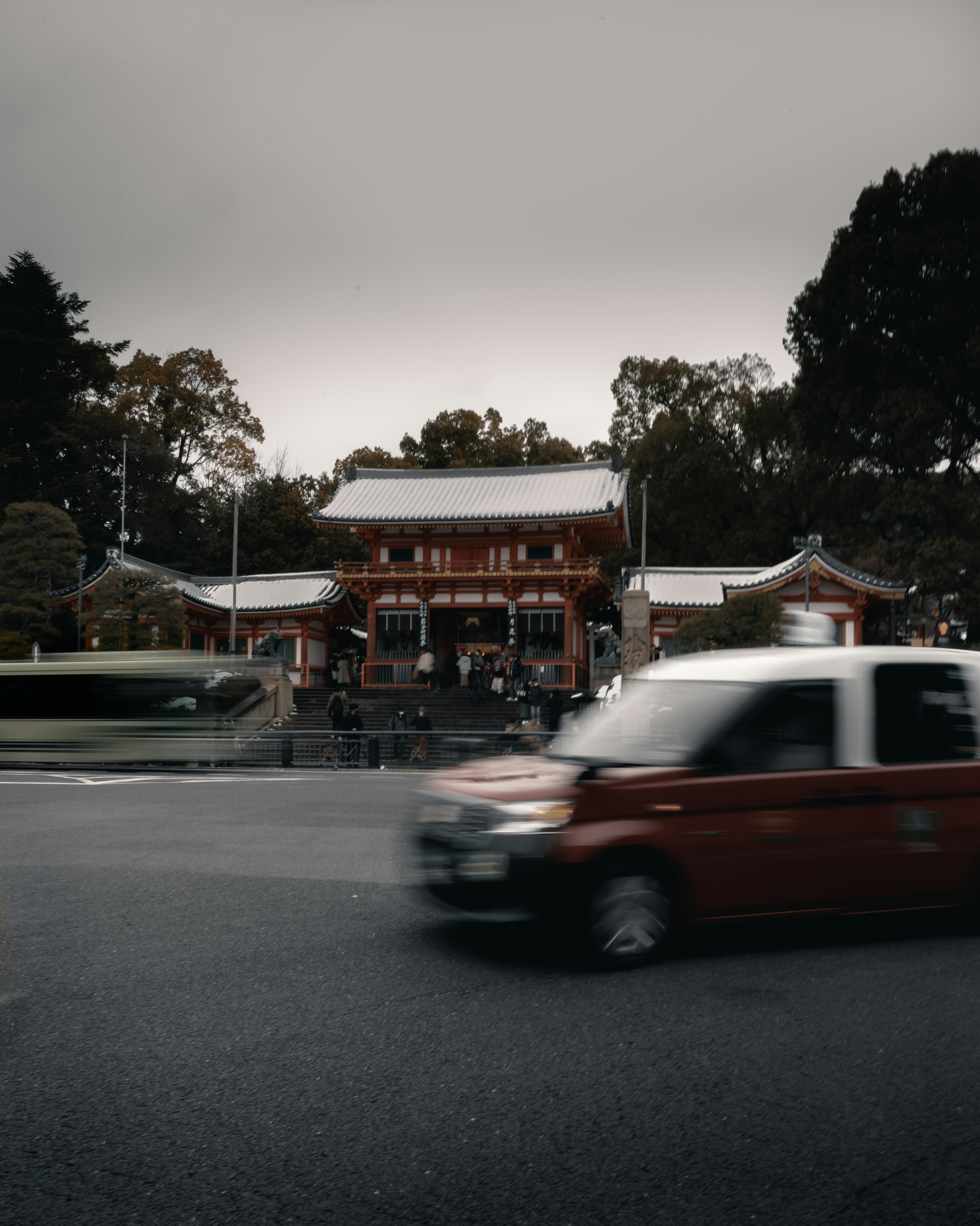 Santuario japonés tradicional bajo un cielo oscuro con un coche rojo en movimiento