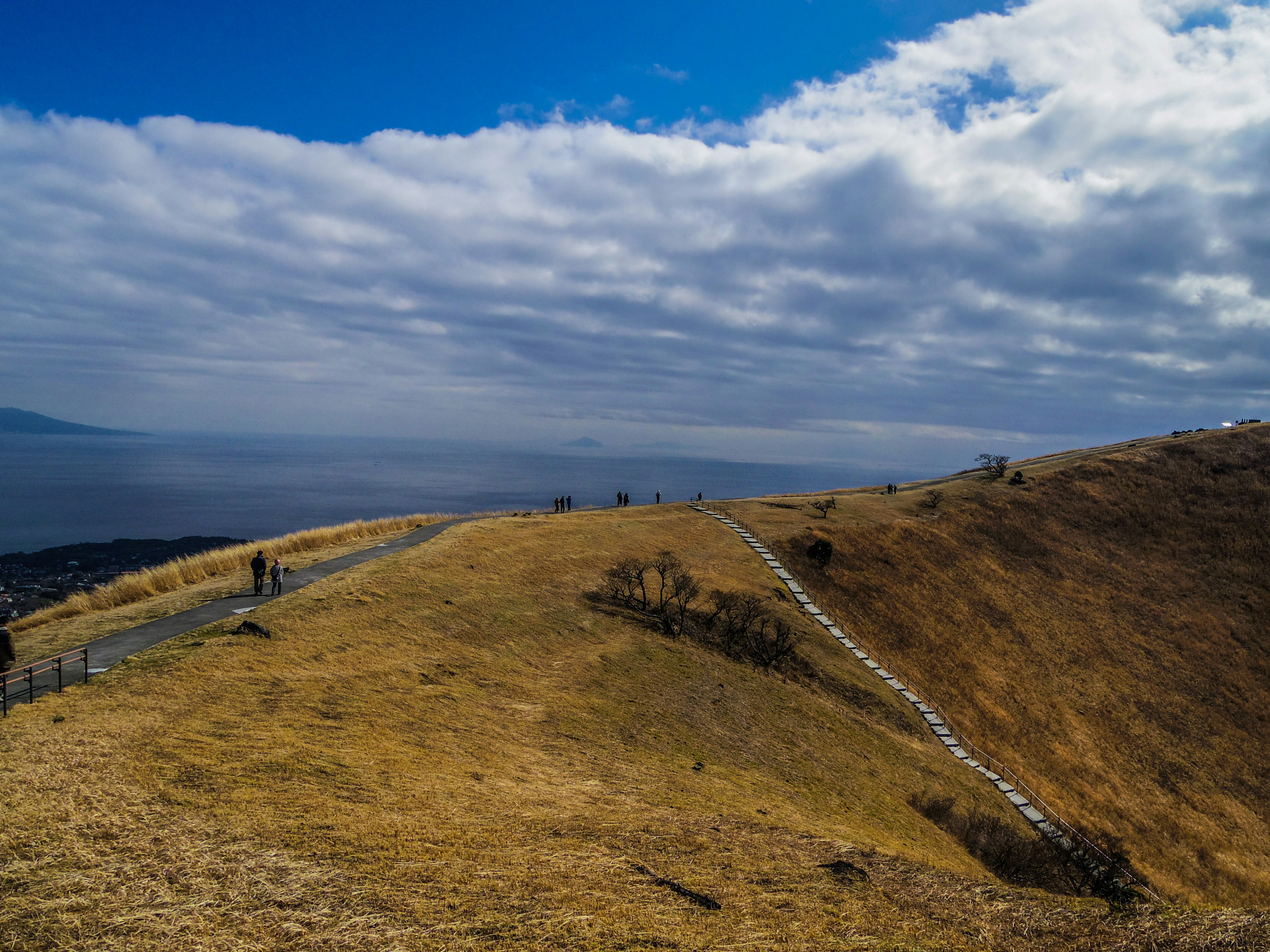 Panoramablick auf einen Hügel unter blauem Himmel mit Wolken mit trockenem Gras und einem gewundenen Weg