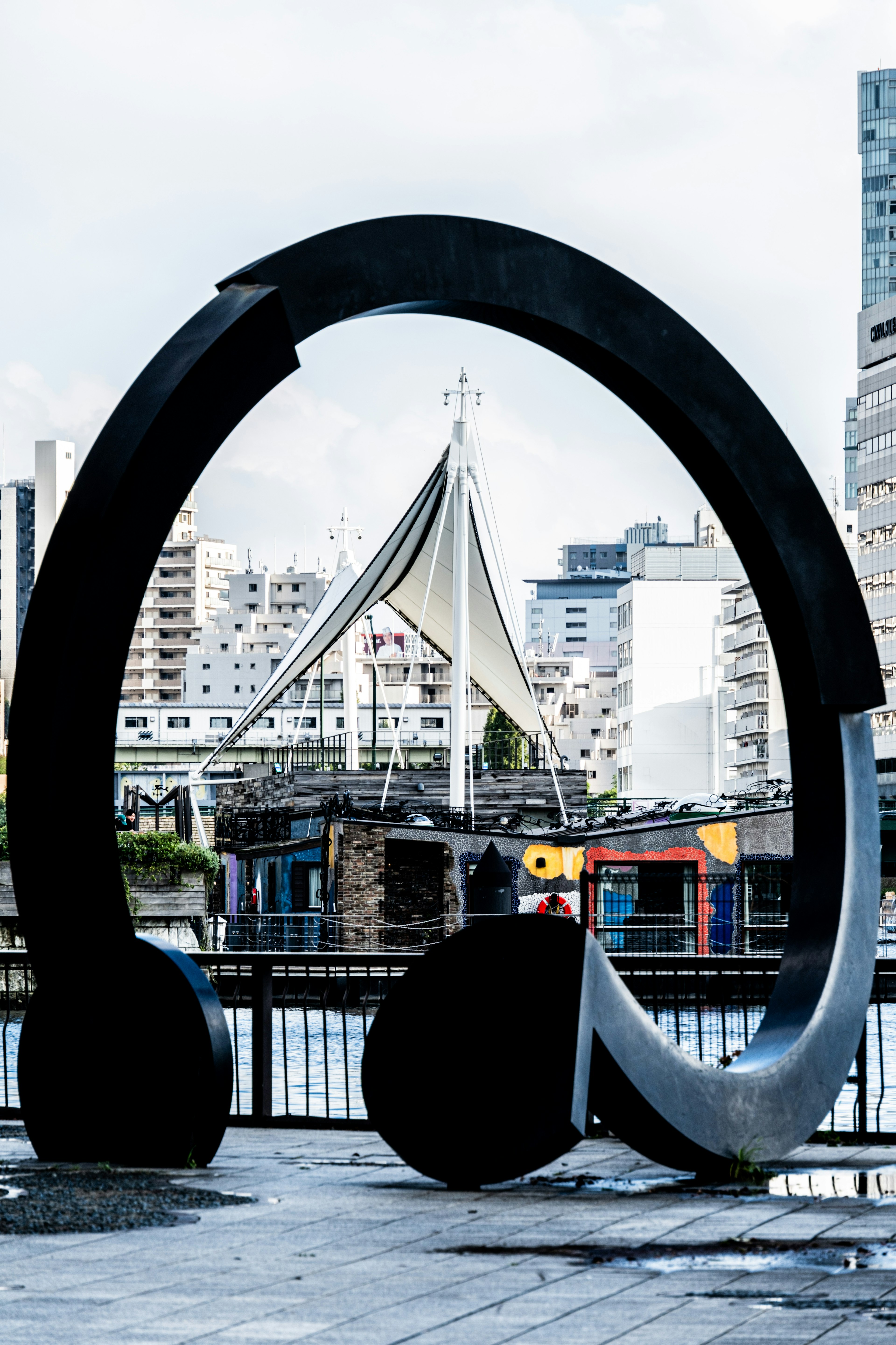 Large black and white headphone sculpture standing by the water with a distinctive building in the background