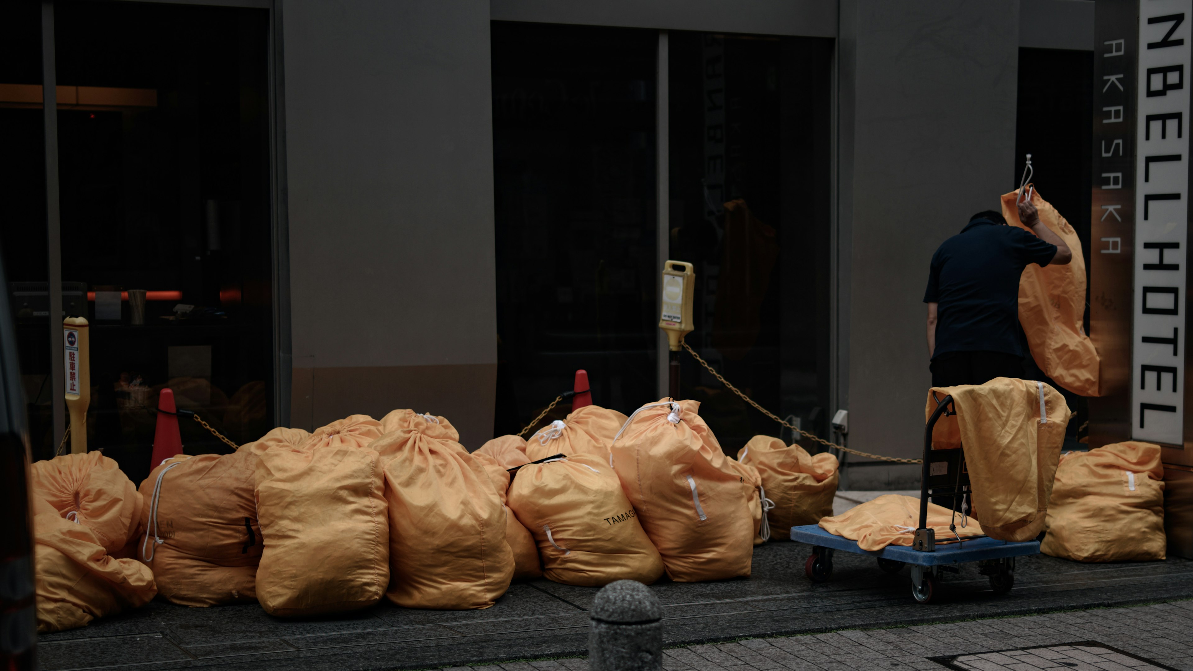 Orange garbage bags stacked in front of a hotel with a worker