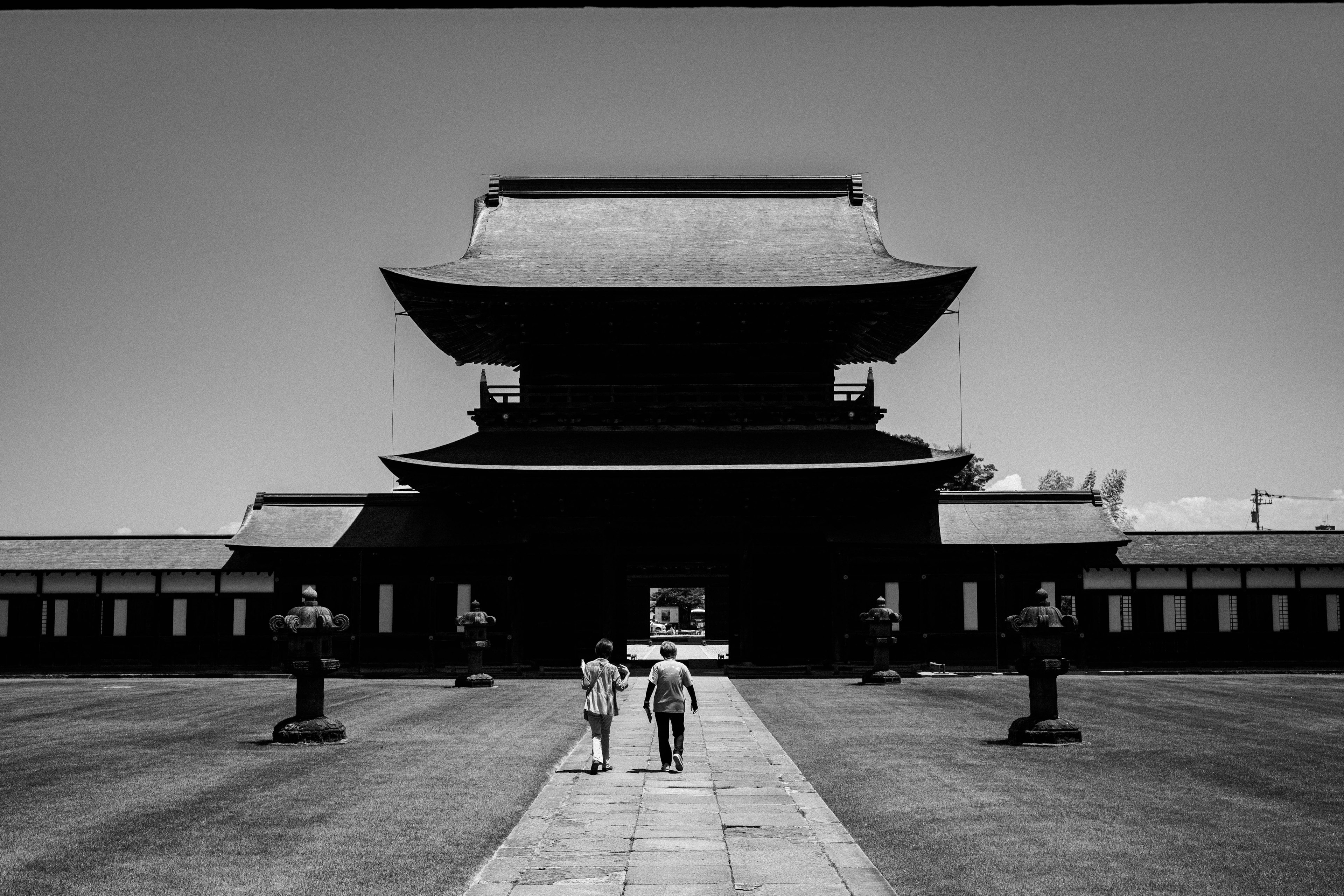 Two people walking in front of a traditional Japanese building in black and white