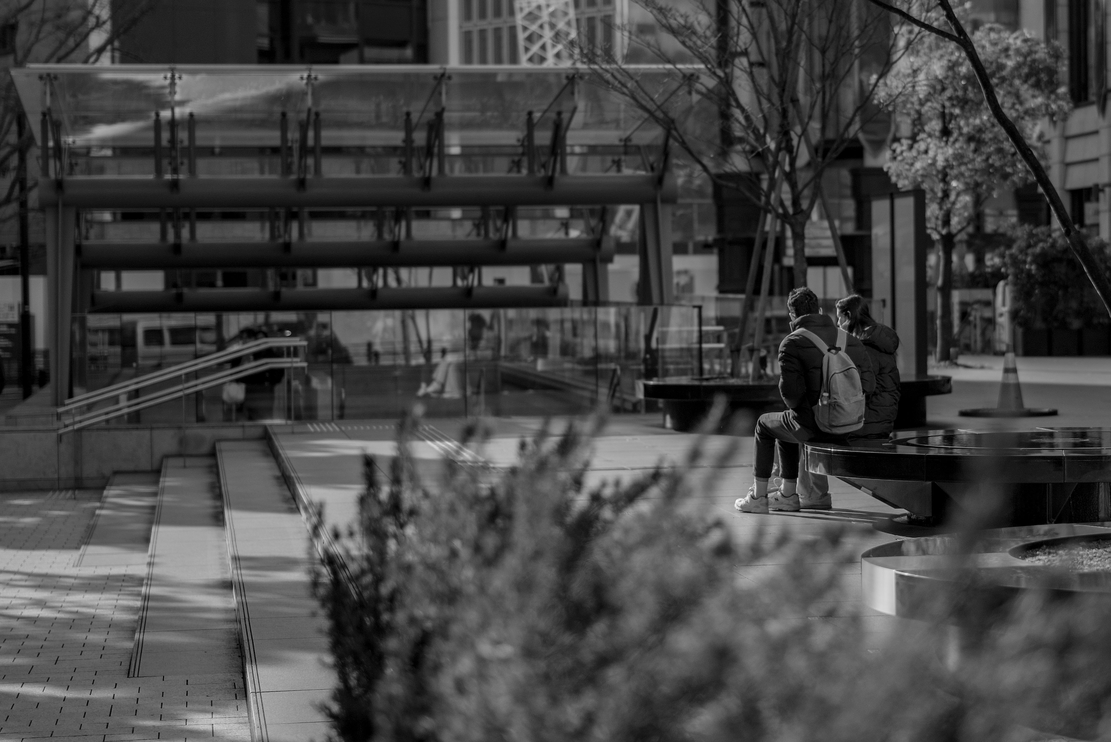 Scène de parc urbain en noir et blanc avec des gens assis sur des bancs et des bâtiments en arrière-plan