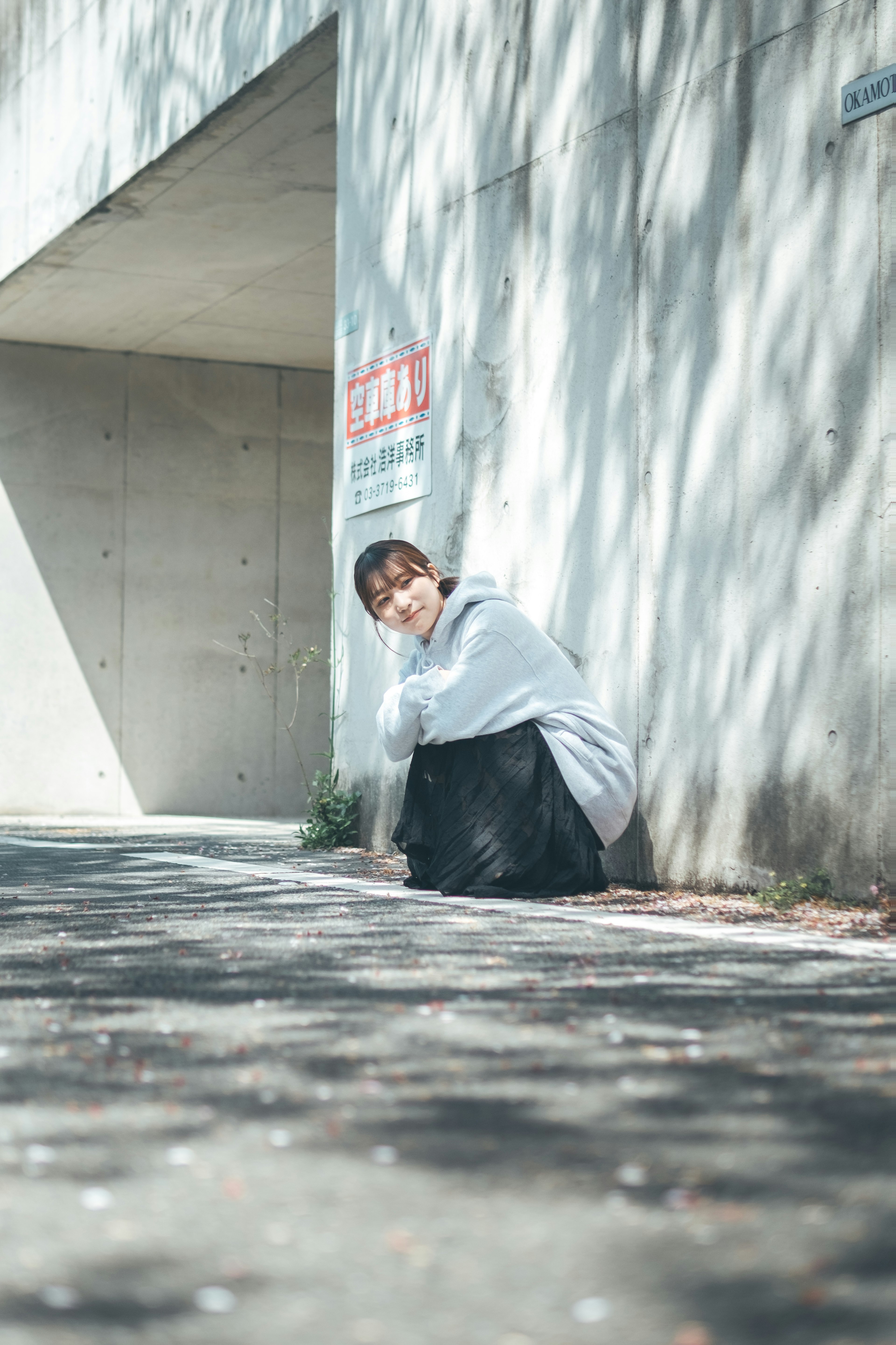 Une femme assise devant un mur en béton avec des ombres douces