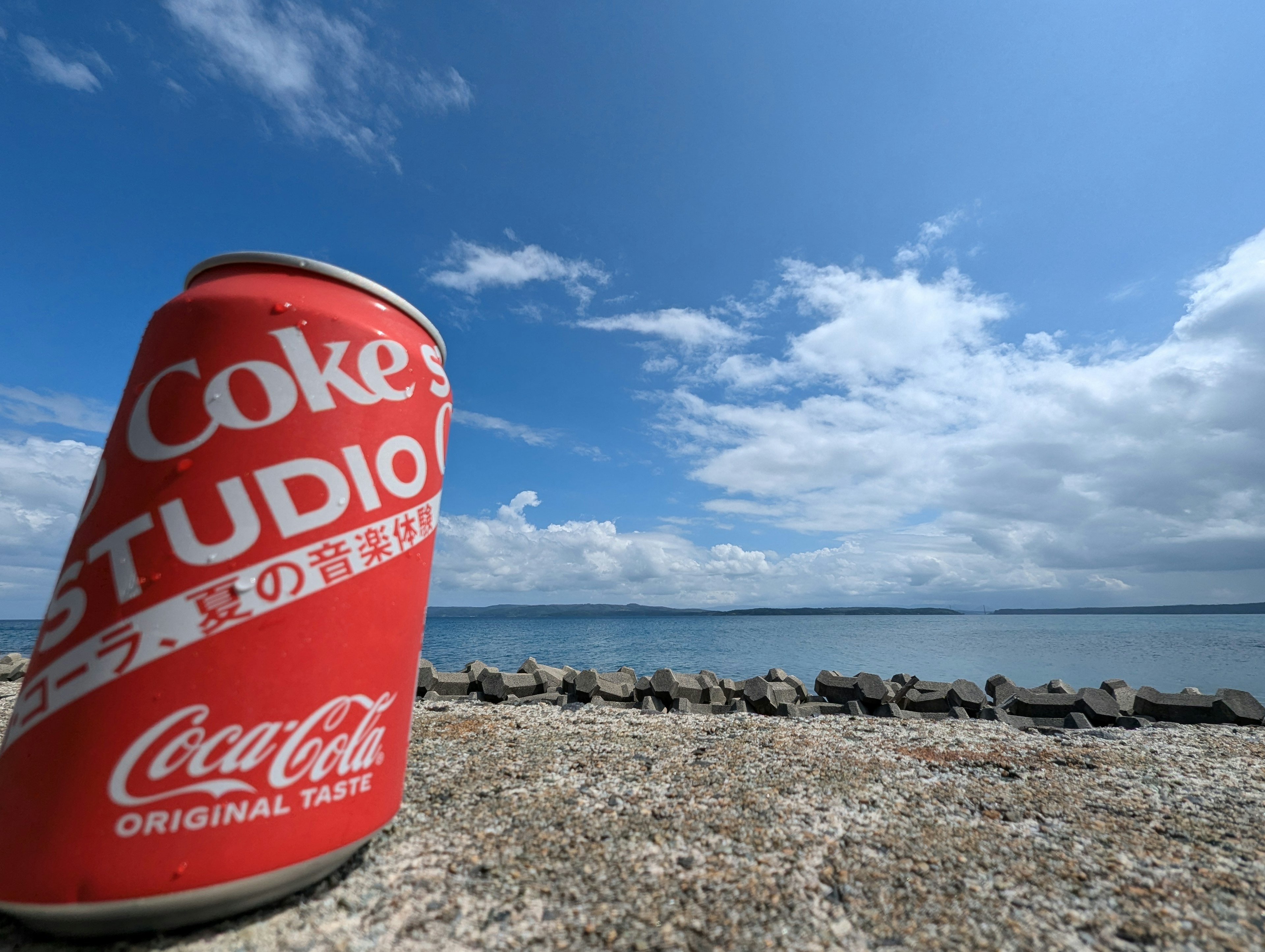 Kaleng Coca-Cola merah di pantai di bawah langit biru