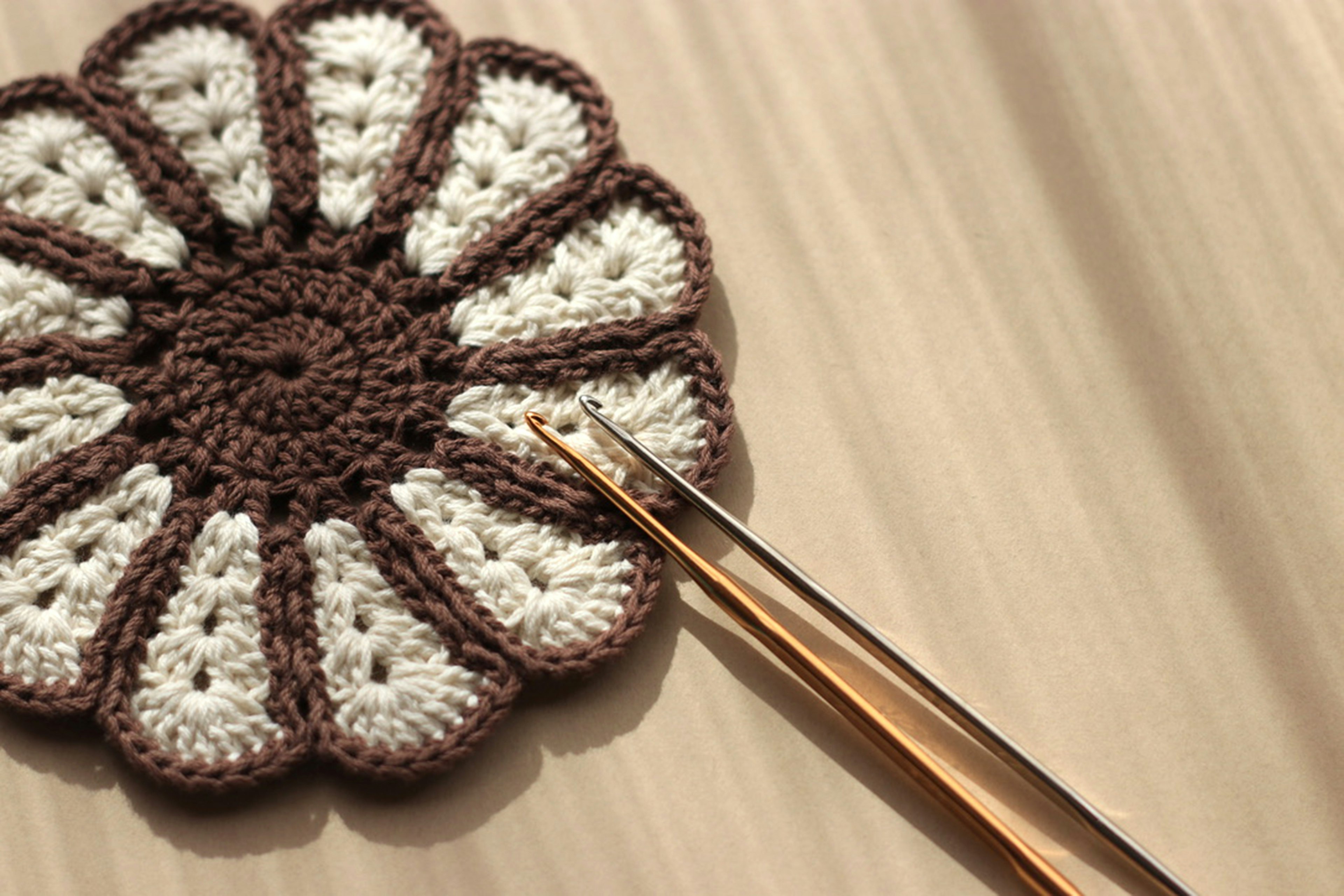 Brown and white flower-patterned crochet coaster with a golden crochet hook