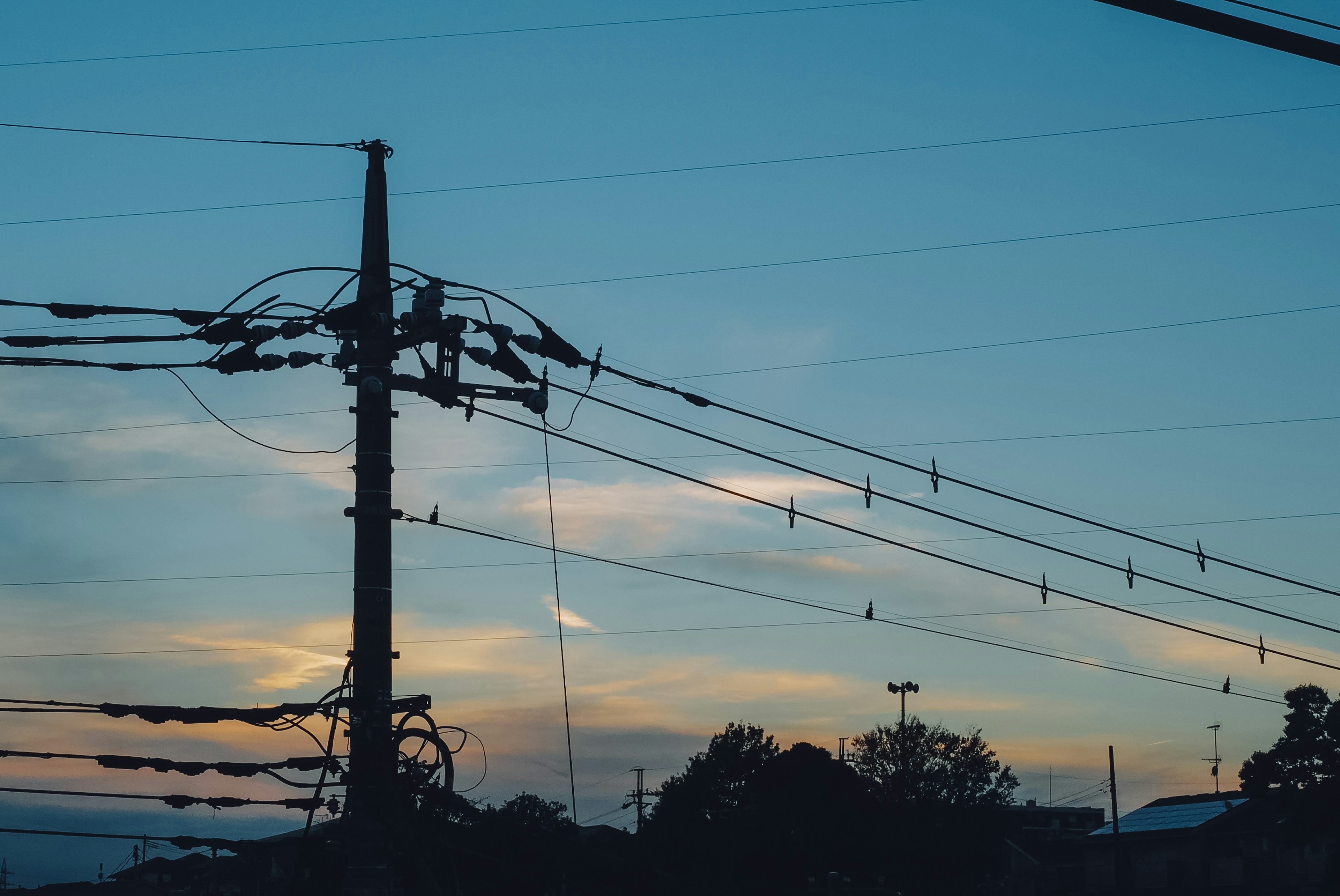 Siluet tiang listrik dan kabel listrik di latar belakang langit senja