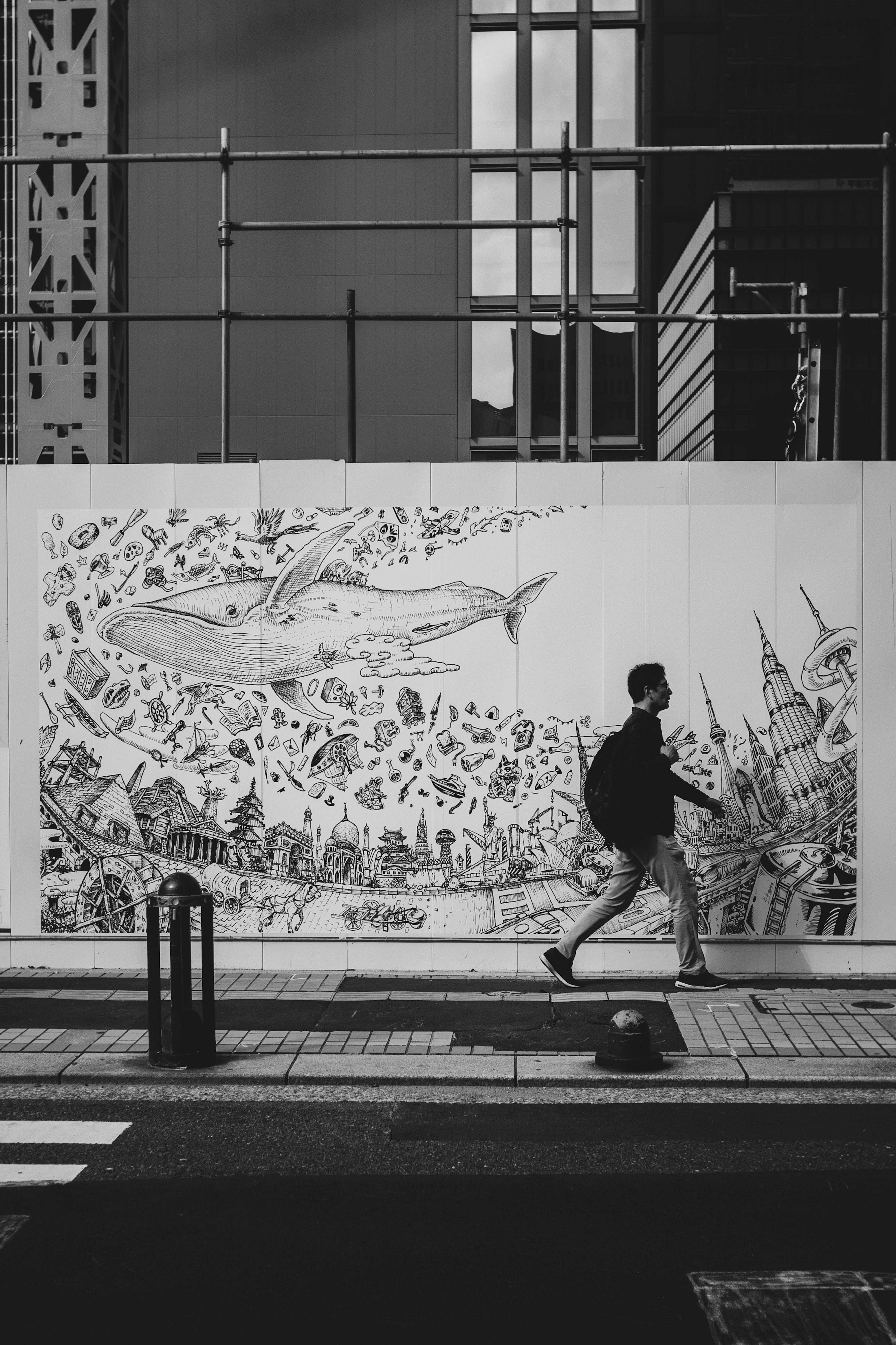 Une personne marchant en noir et blanc devant une fresque représentant une baleine et un paysage urbain