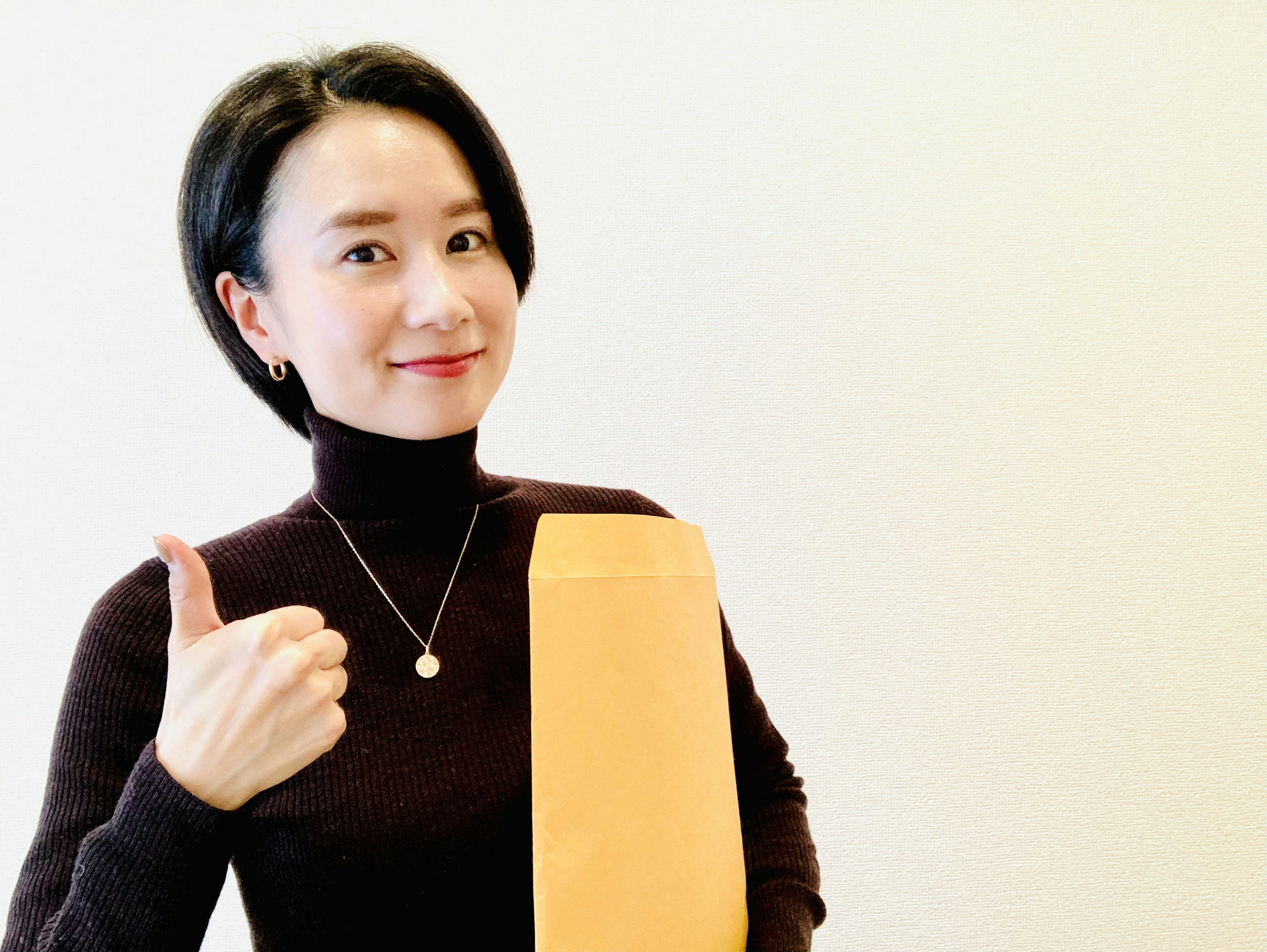 Woman in brown sweater holding an envelope and giving a thumbs up