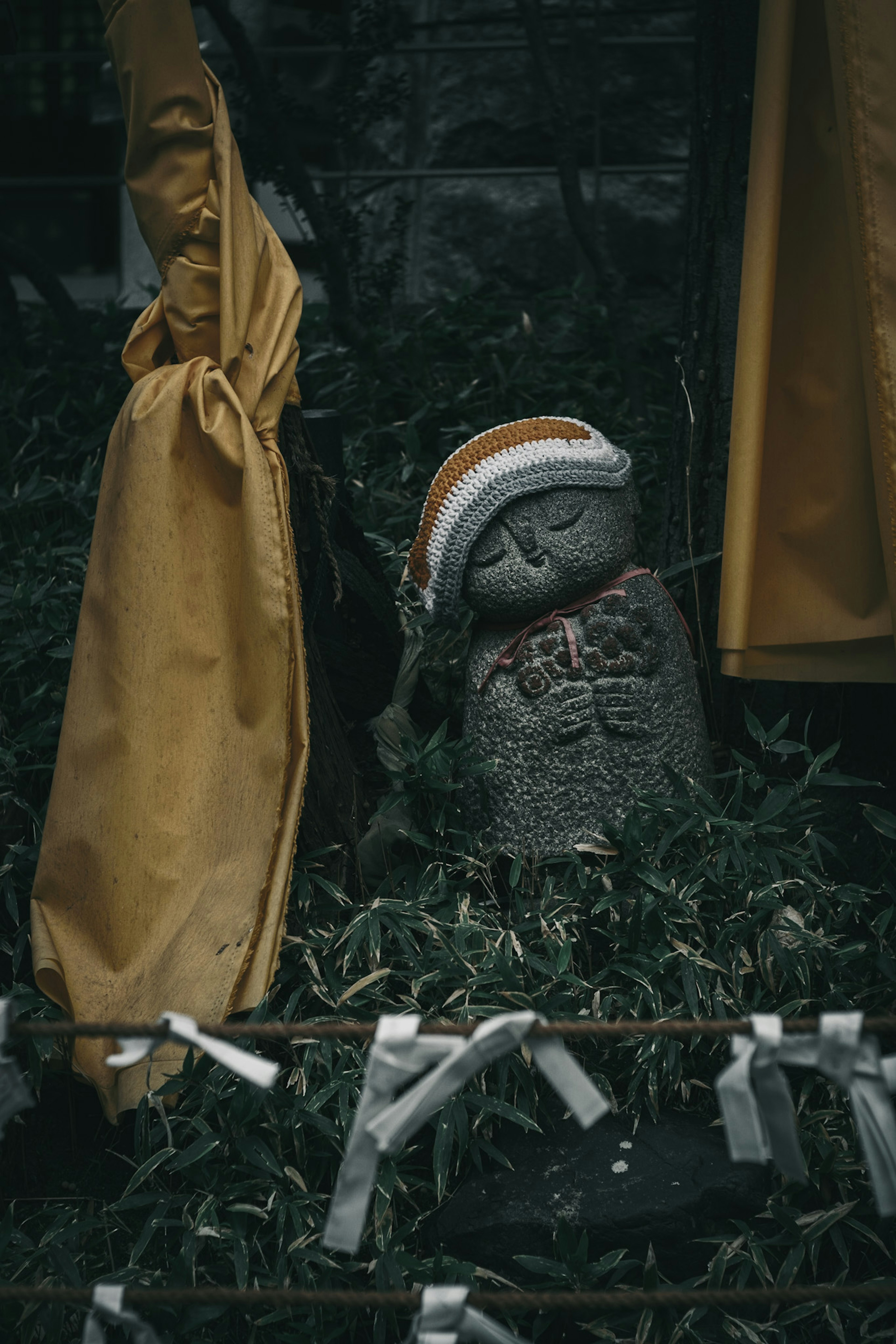 Statue en pierre d'un enfant entourée de plantes vertes et d'un parapluie jaune