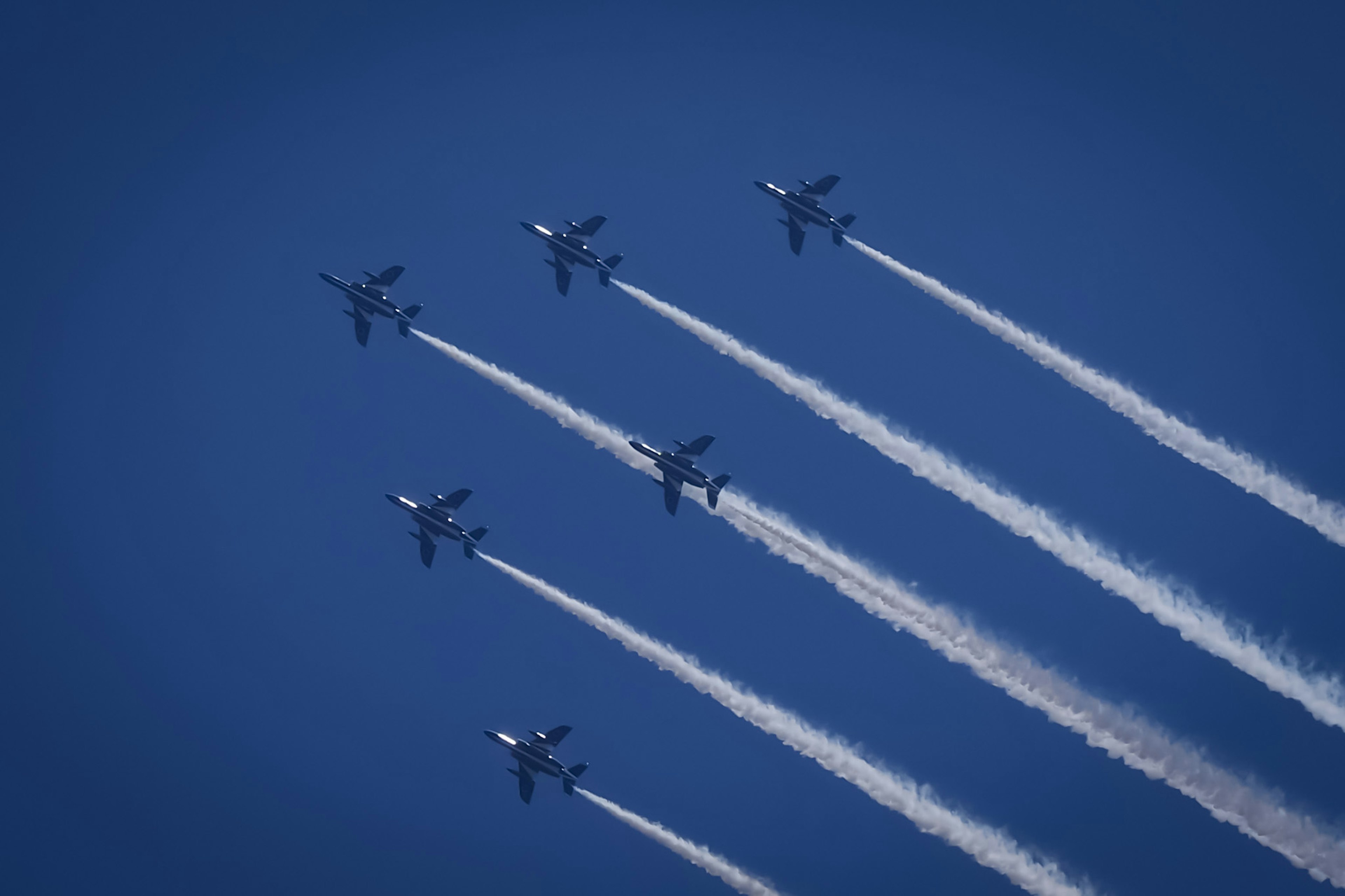 Formation of aircraft flying in blue sky leaving white vapor trails