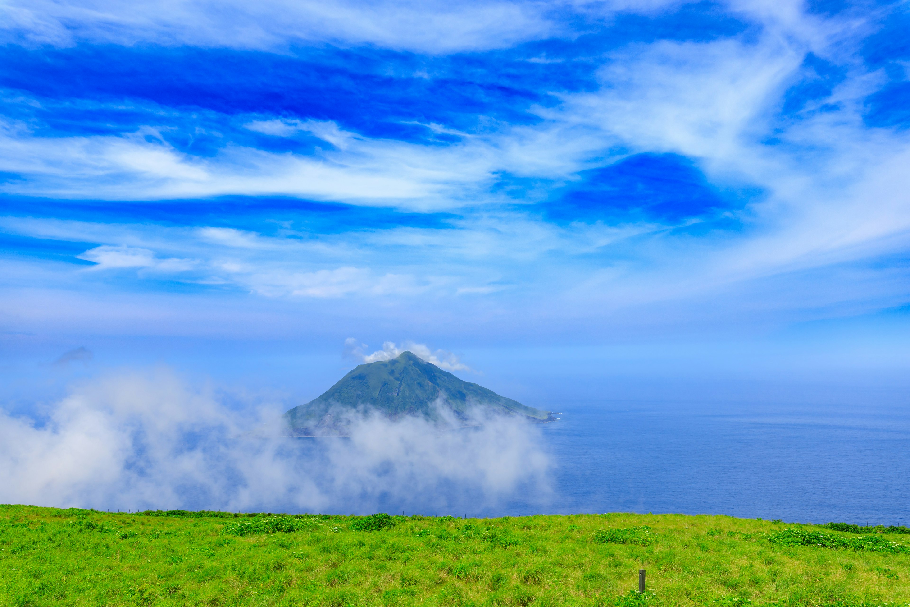 Una pequeña isla rodeada de cielo azul y nubes sobre un prado verde