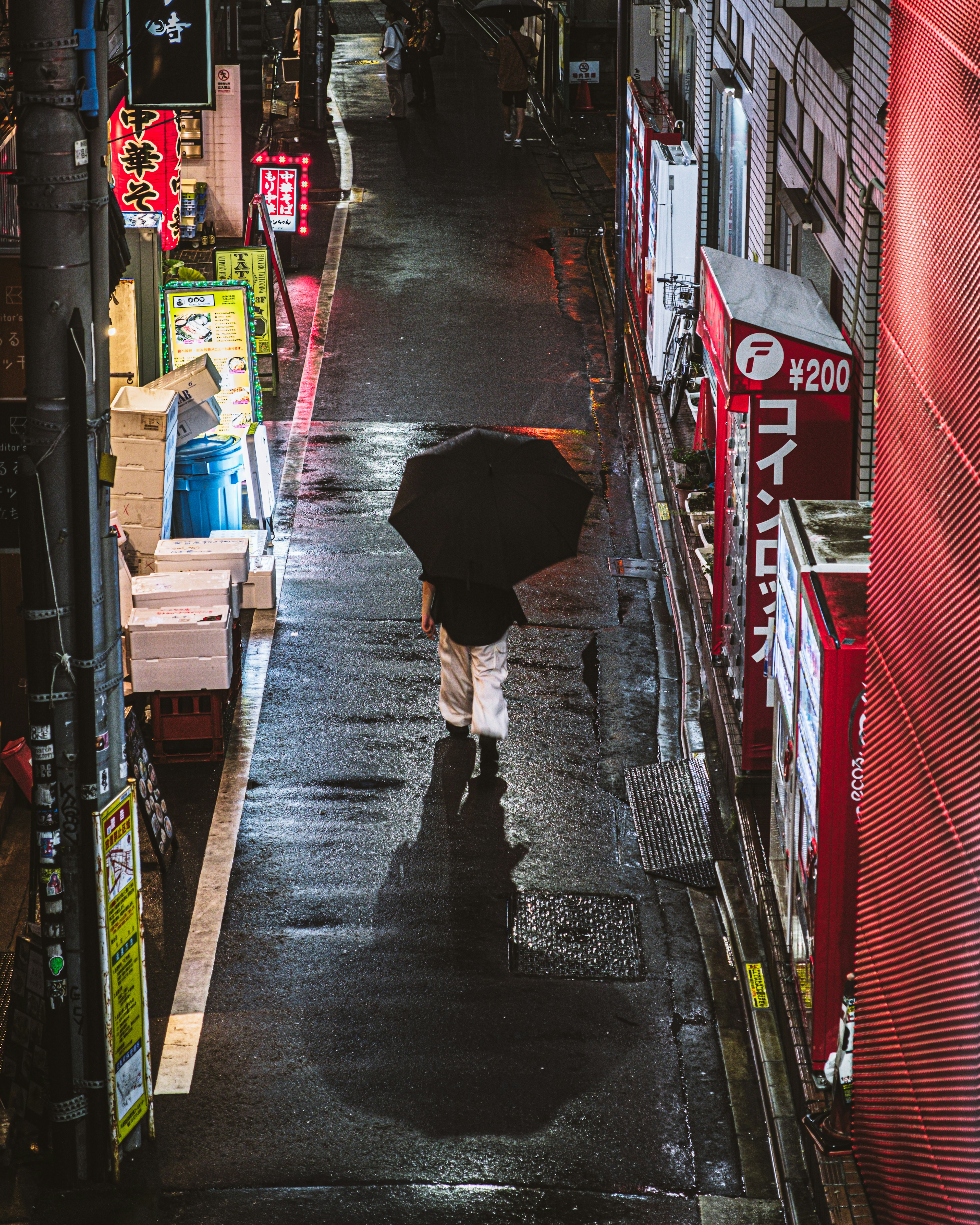 Eine Person, die mit einem Regenschirm in einer engen Gasse nachts im Regen geht