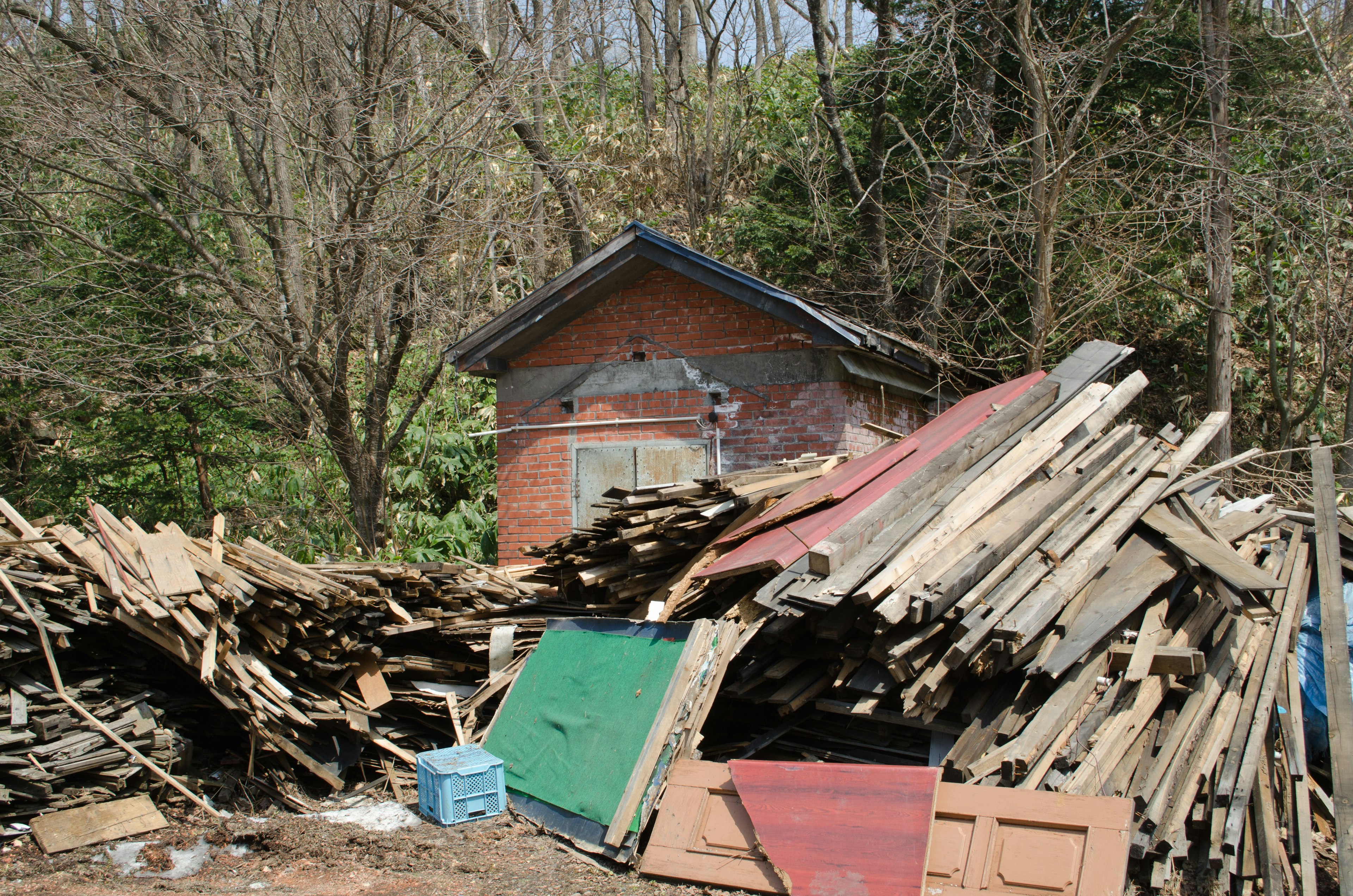 A landscape featuring a pile of wooden planks beside an old house