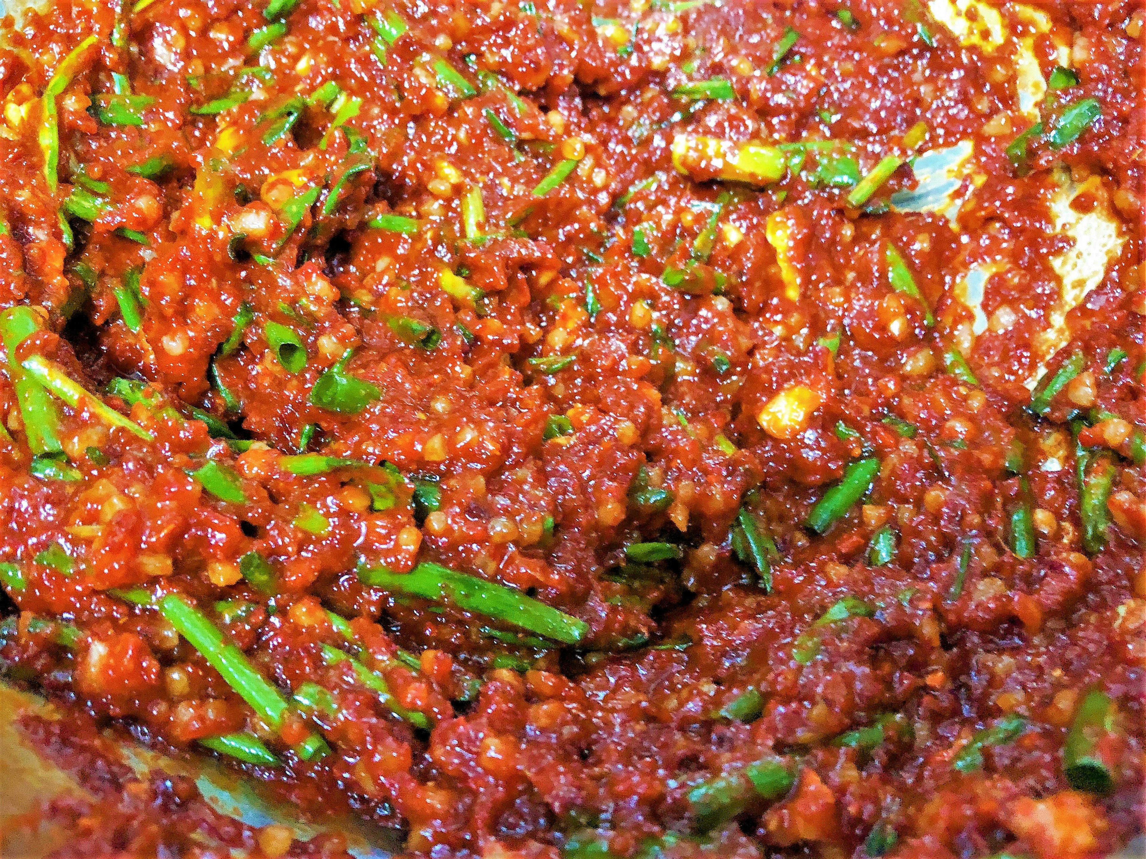 A mixture of red sauce and finely chopped green onions in a bowl