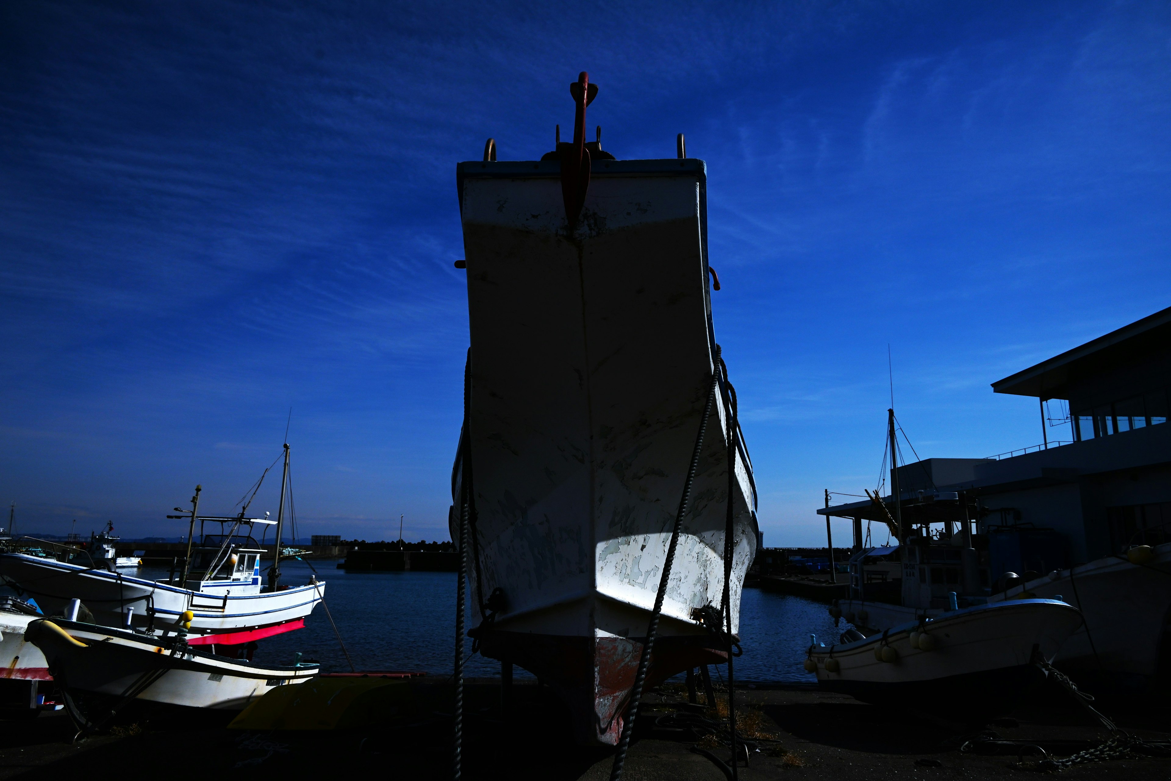 Silhouette of a boat under a blue sky with surrounding smaller boats